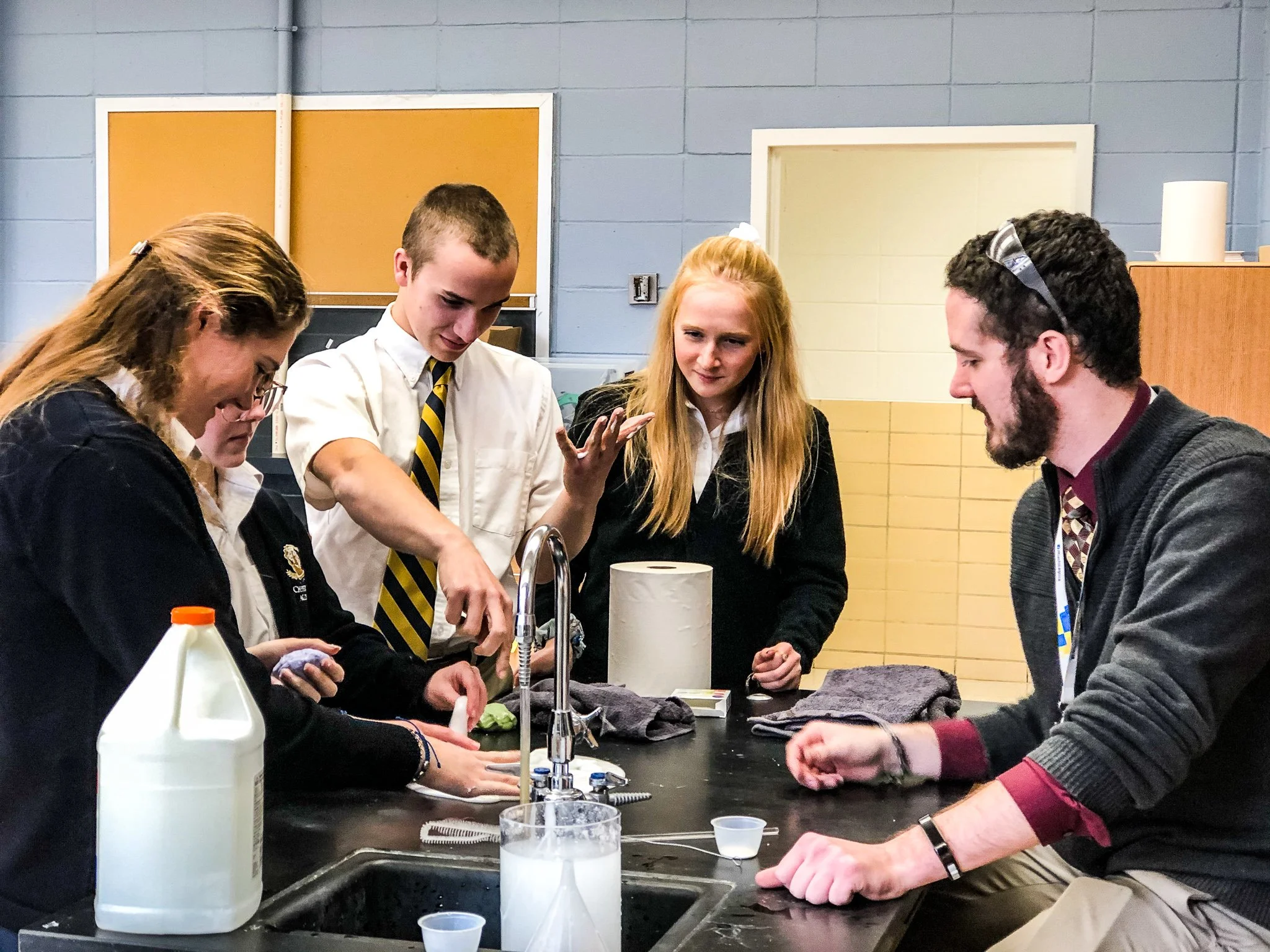 A group of students in school uniforms gathered around a laboratory table doing a science experiment with various lab equipment.