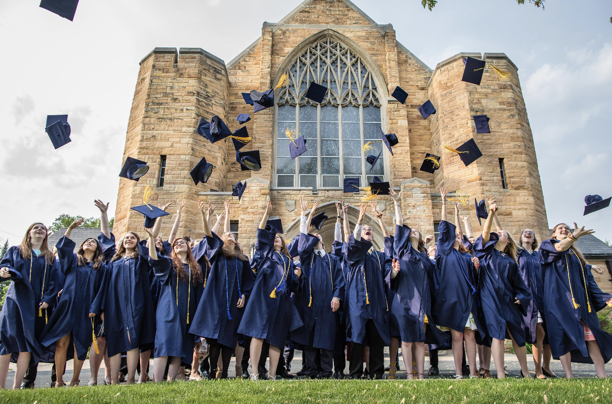 Graduates in caps and gowns celebrating outside a church as they toss their caps into the air.