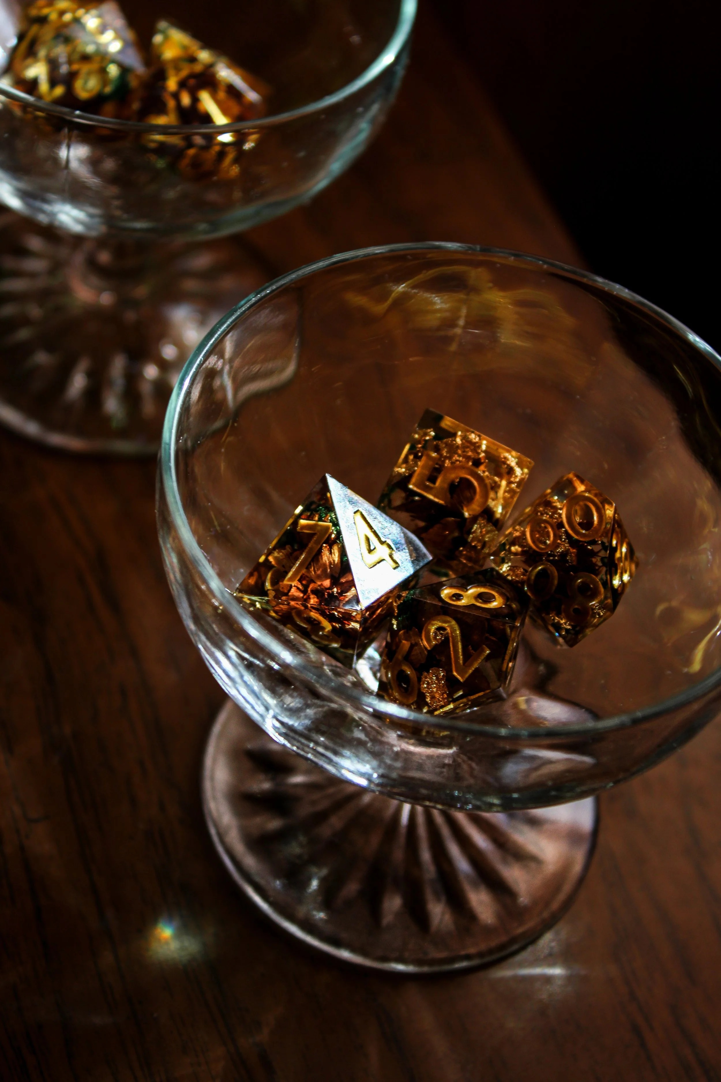 Close-up of a glass with gold-colored '10' and '20' dice inside on a wooden surface.