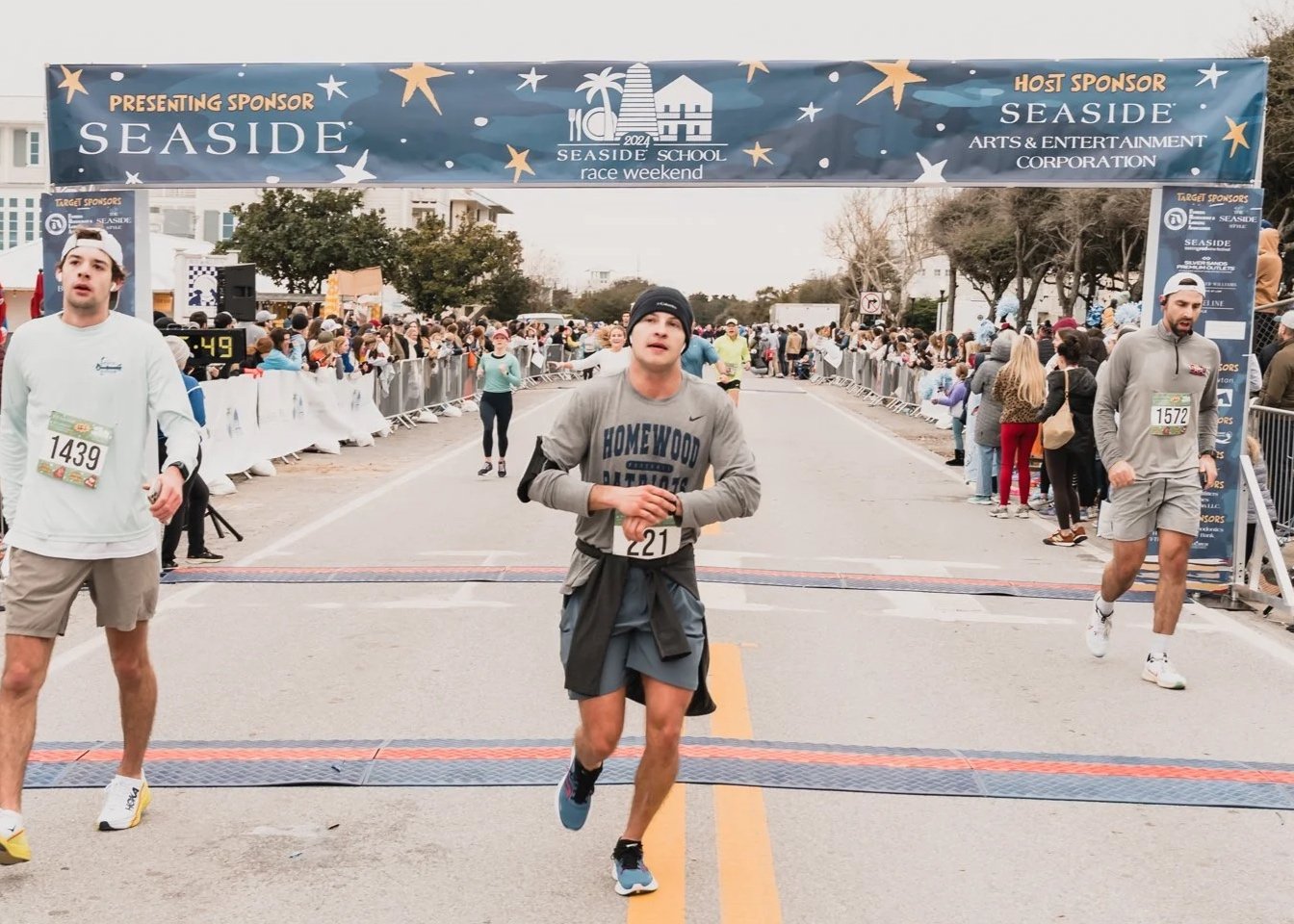 Runners crossing the finish line at a marathon event, with spectators on the sides and a banner overhead reading 'Seaside School Race Weekend 2024'.