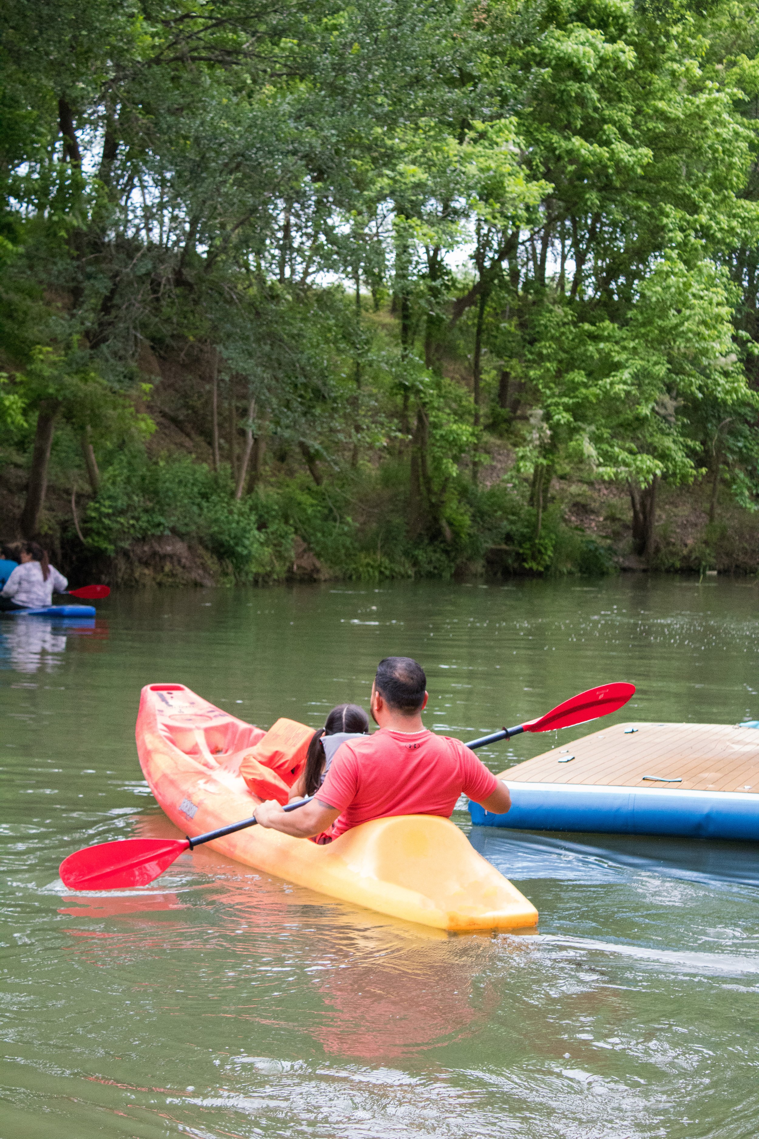 People kayaking on a river surrounded by green trees.