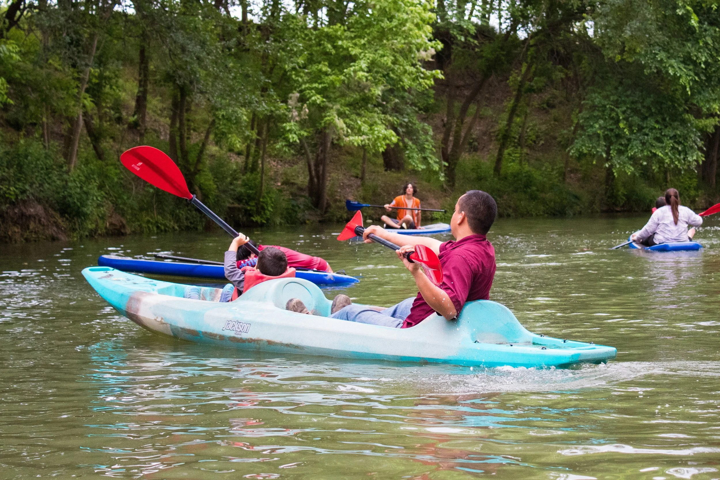 People kayaking on a calm river surrounded by green trees.
