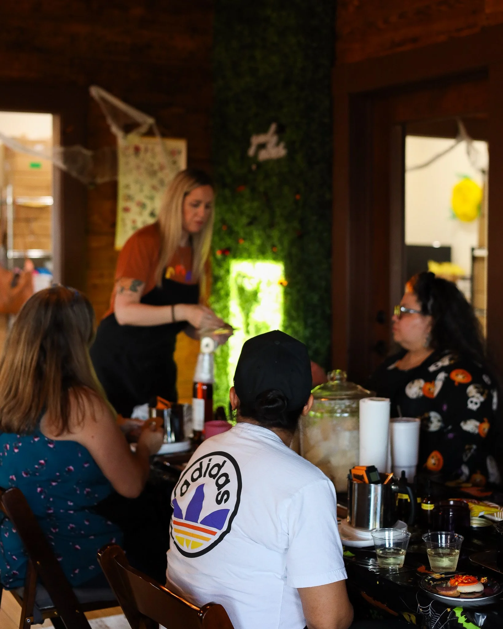 People gathered at a table inside for Halloween-themed celebration, with decorations and treats on the table.