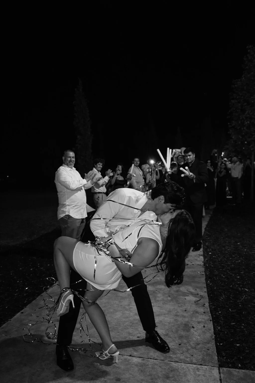 A couple sharing a kiss in front of a large white castle with turrets, a fountain with statues, and a landscaped garden.
