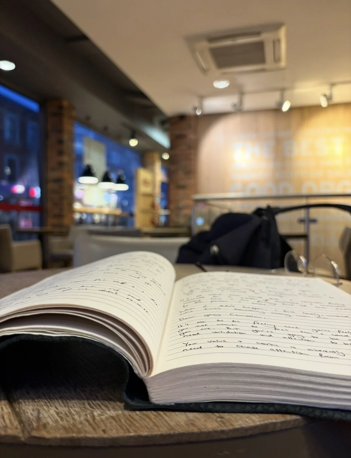 Open notebook with handwritten notes on a table inside a cozy cafe with brick walls, pendant lights, and a blurred background.