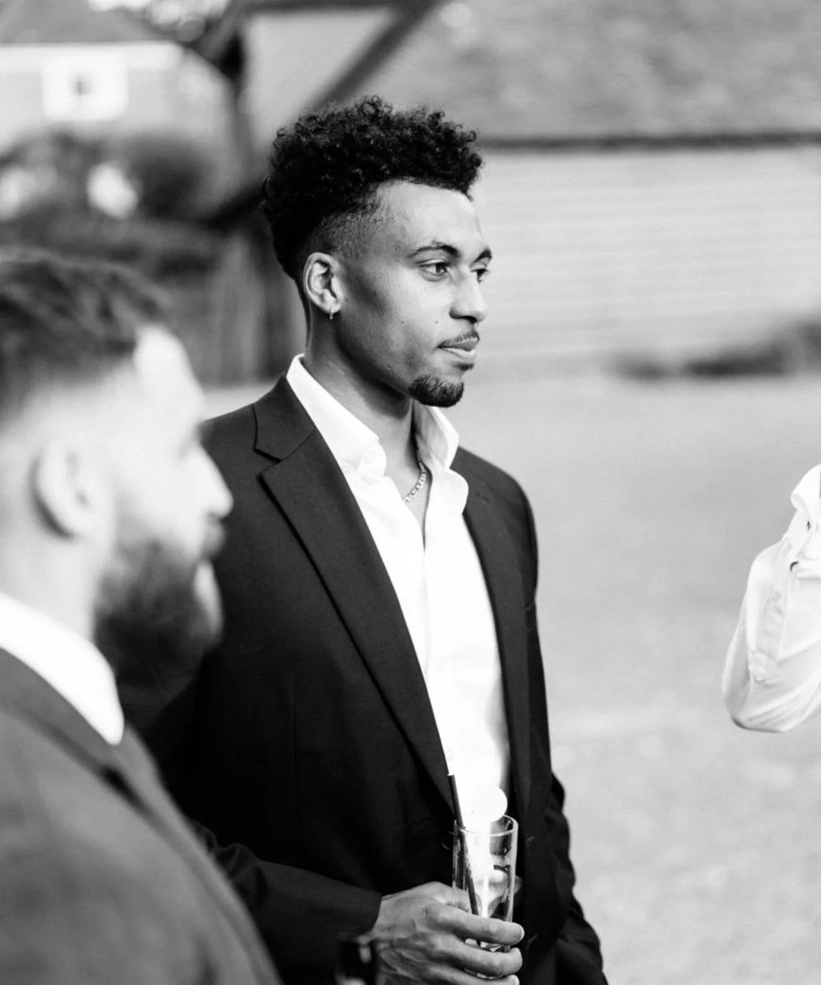 A man in a suit holding a glass, standing outdoors during a social event