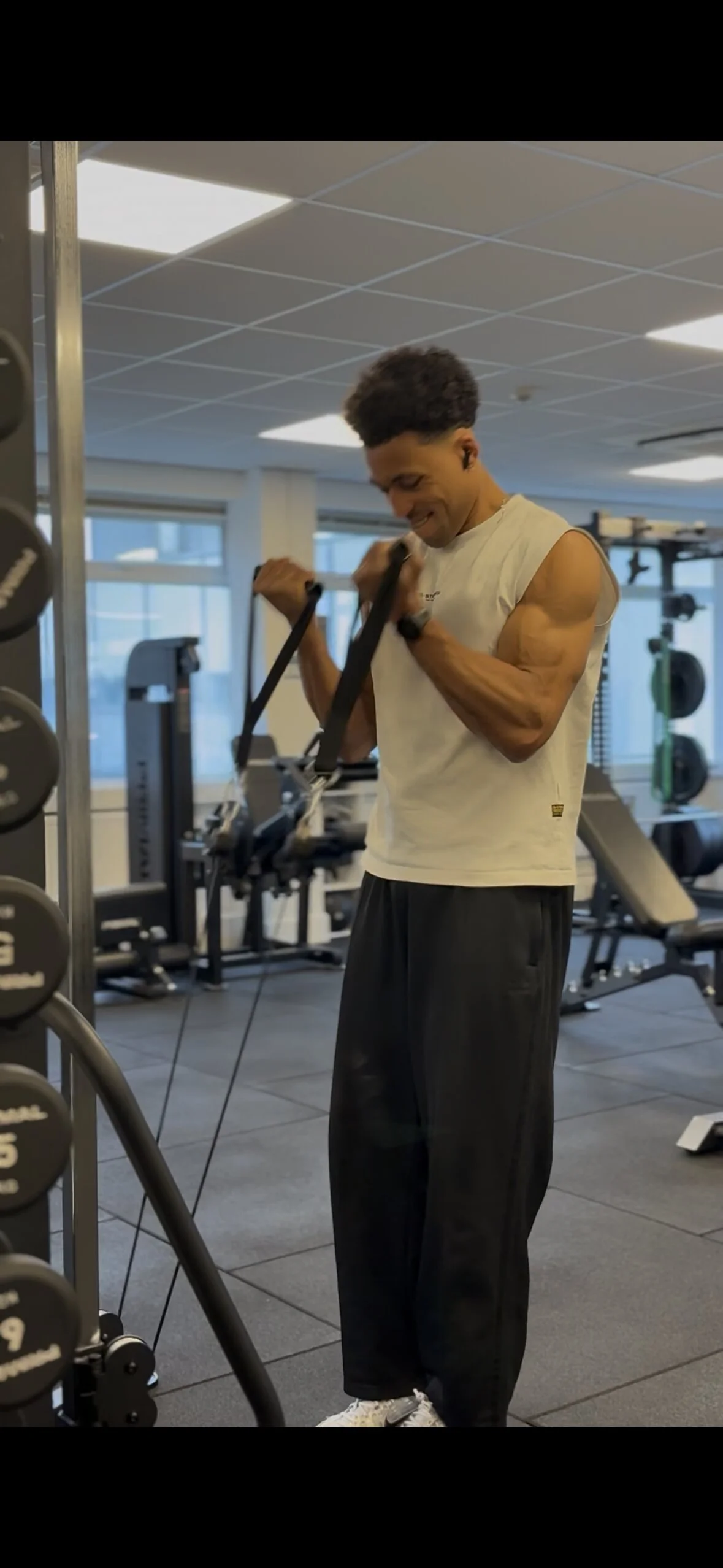 A young man working out in a gym using a resistance band, wearing a sleeveless shirt and black pants.