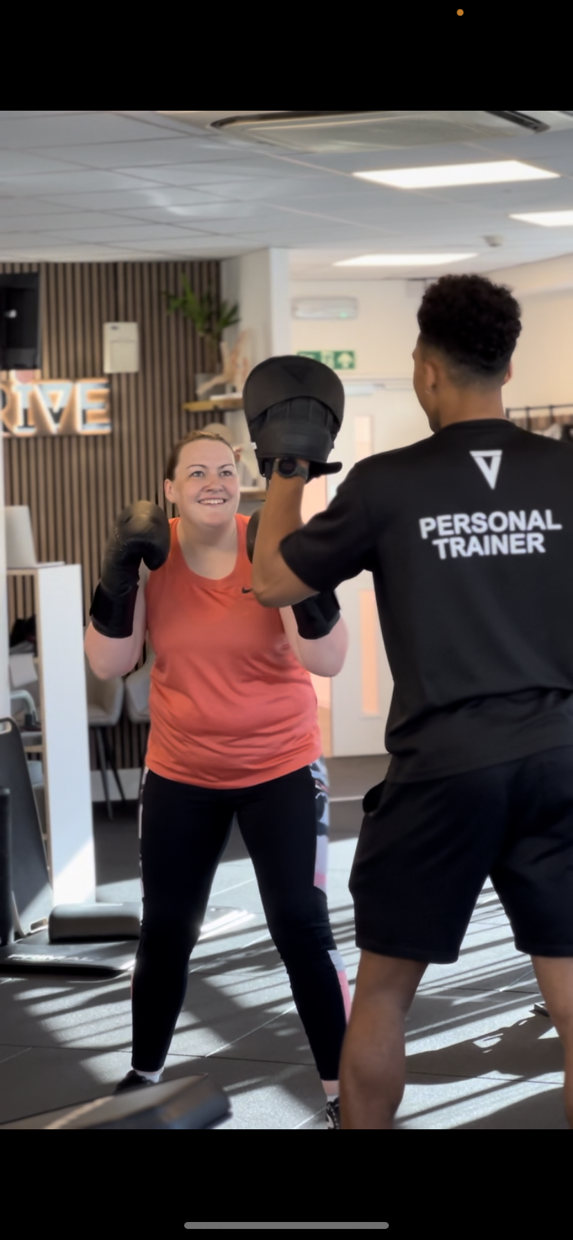Woman in red tank top boxing with a trainer in a gym.