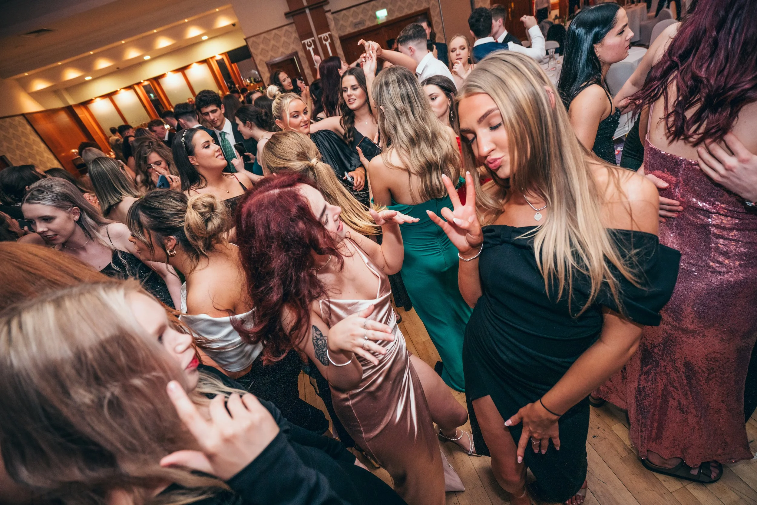 People dancing and socializing at a party or celebration in an indoor venue with wooden floors.