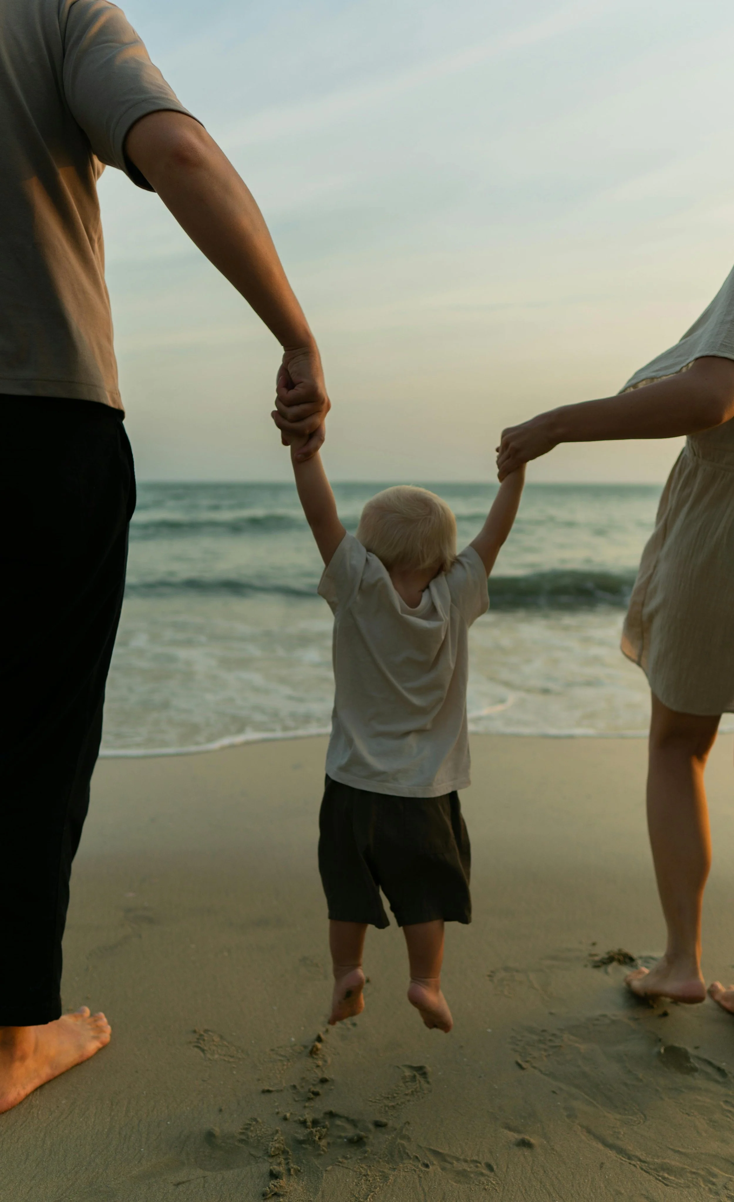 Family holding hands walking on the beach at sunset, with visible footprints in the sand.