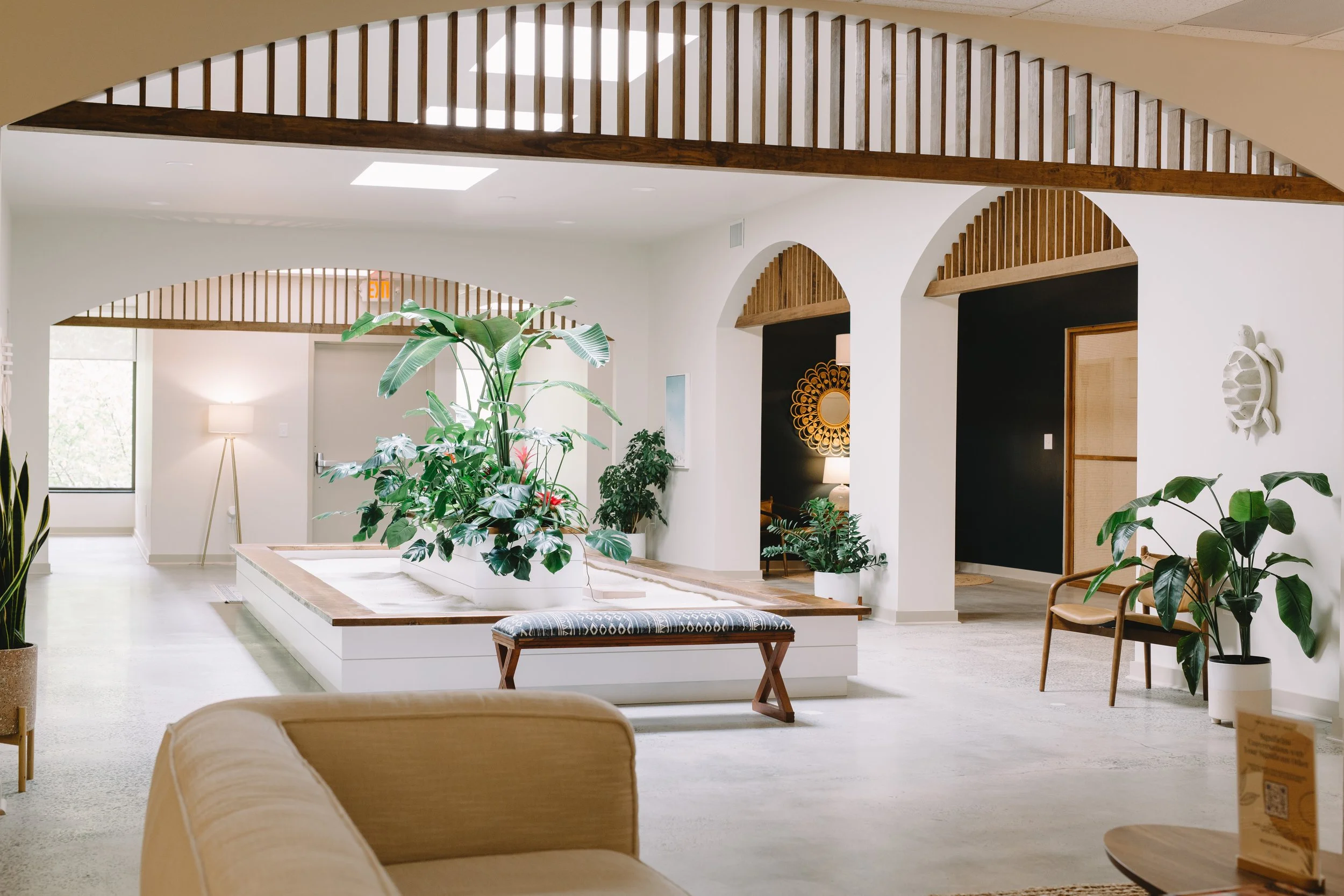 Interior of a modern, well-lit lobby with large green plants, wooden accents, and seating areas with a neutral color palette.