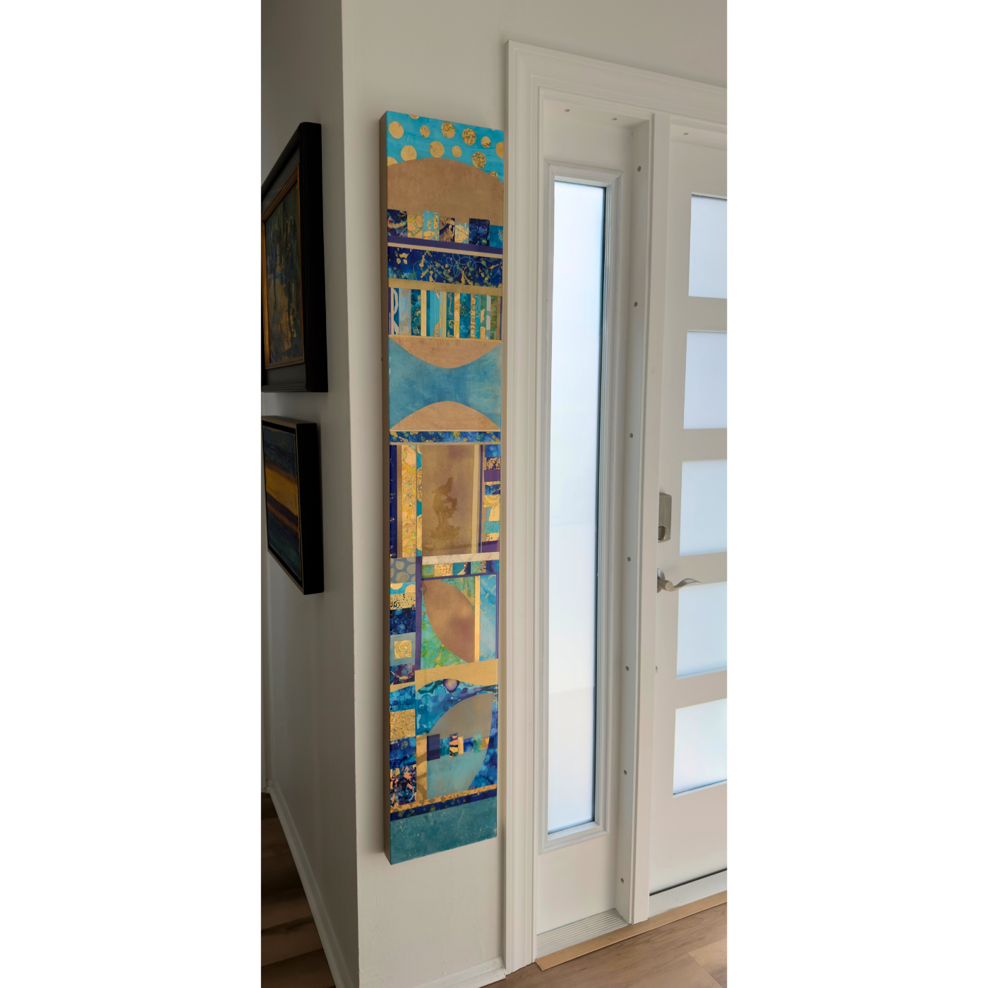 Vertical abstract painting next to a white door with frosted glass panels, on a white wall with other framed artwork.