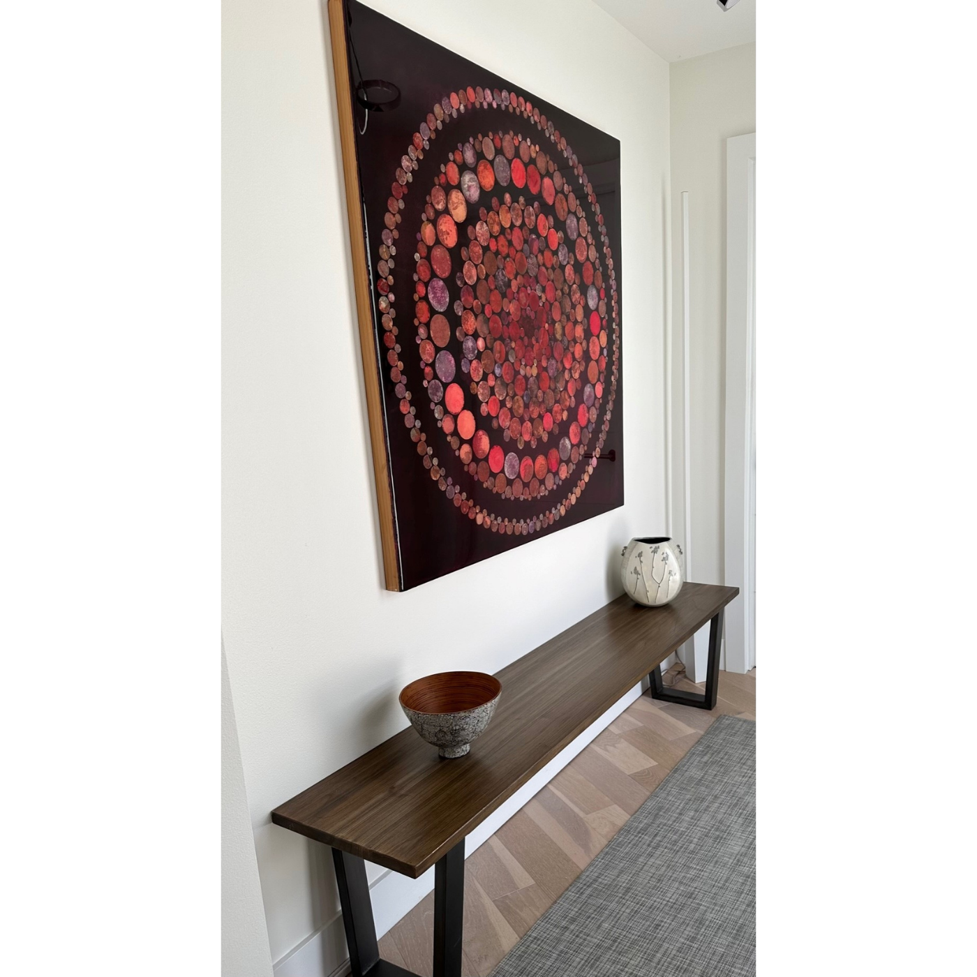 Interior of a room featuring a wooden console table with decorative bowls and a large framed circular artwork by Louise Belcourt hanging on the wall.