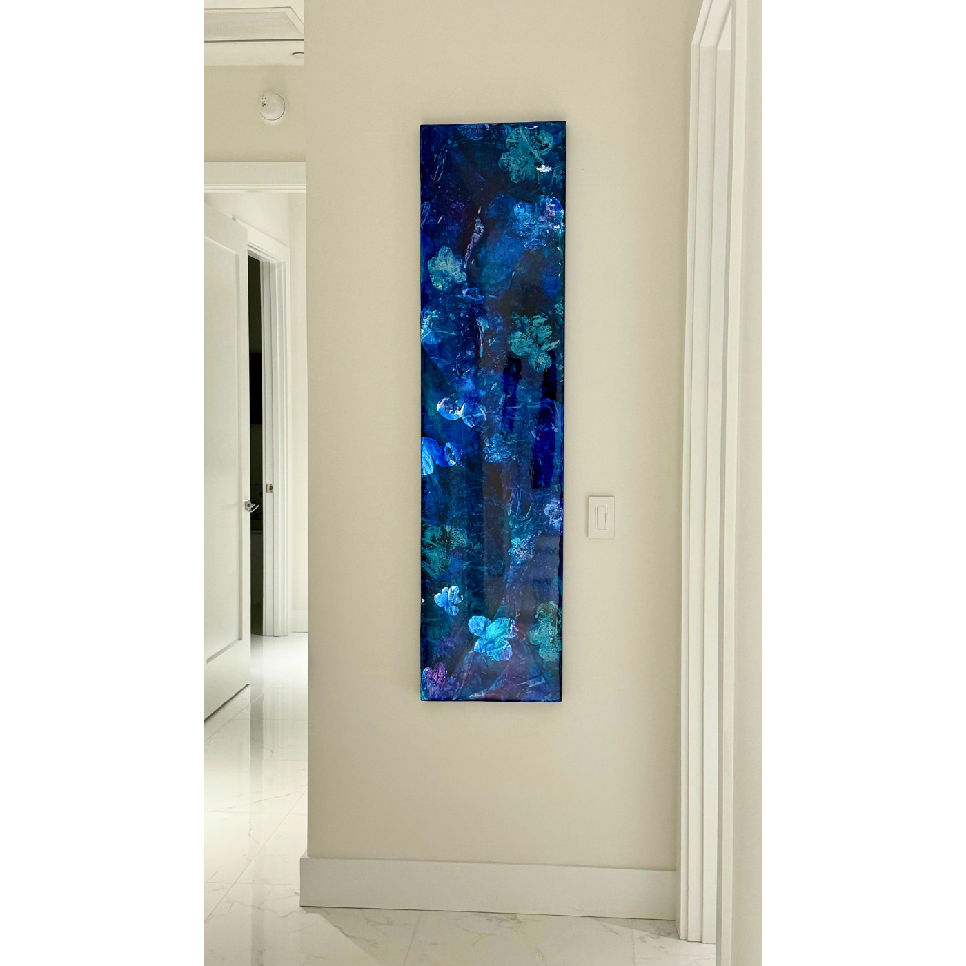Vertical abstract painting with blue hues and floral patterns on a beige wall in a modern interior.