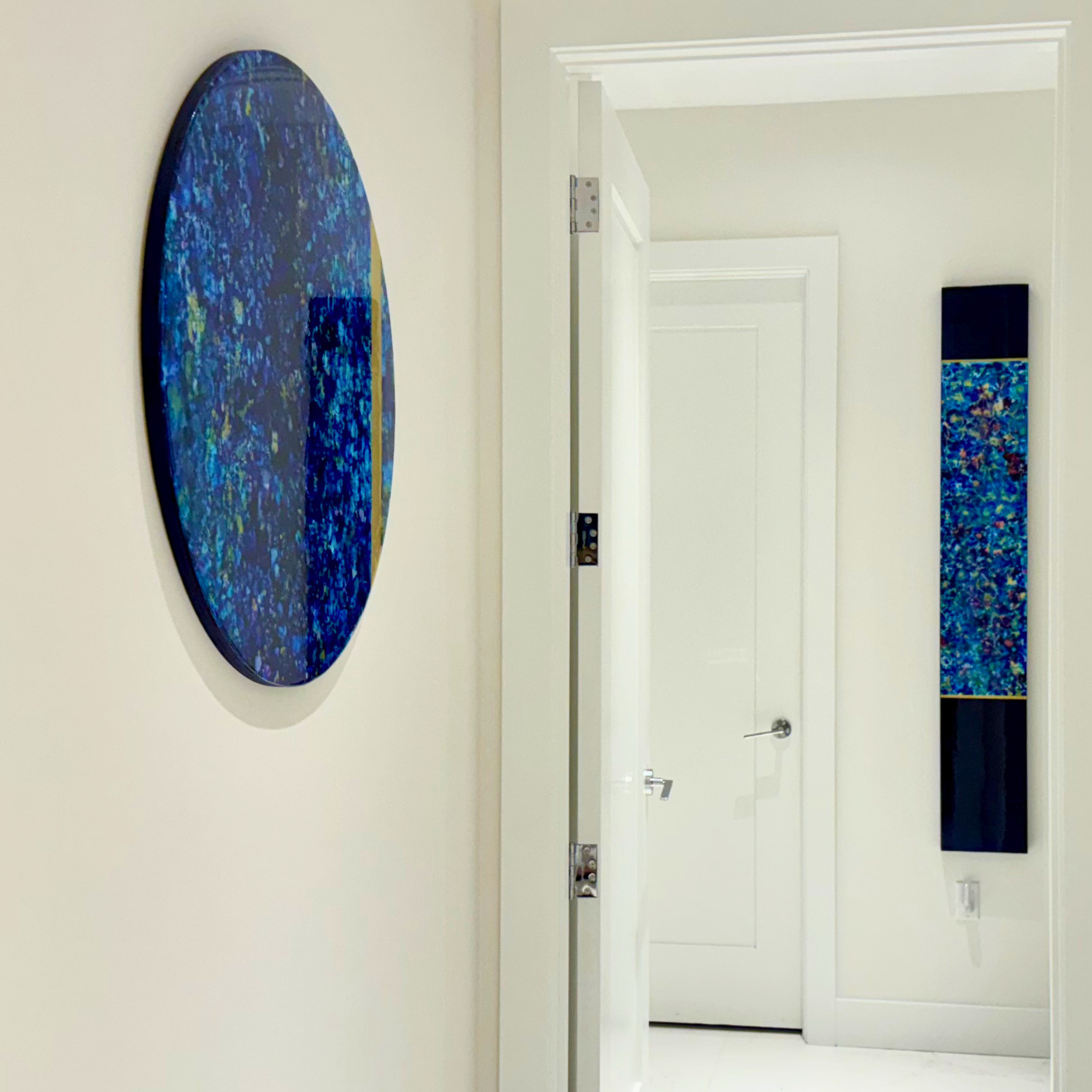 Art gallery hallway with two blue abstract paintings on white walls, one circular and one rectangular.