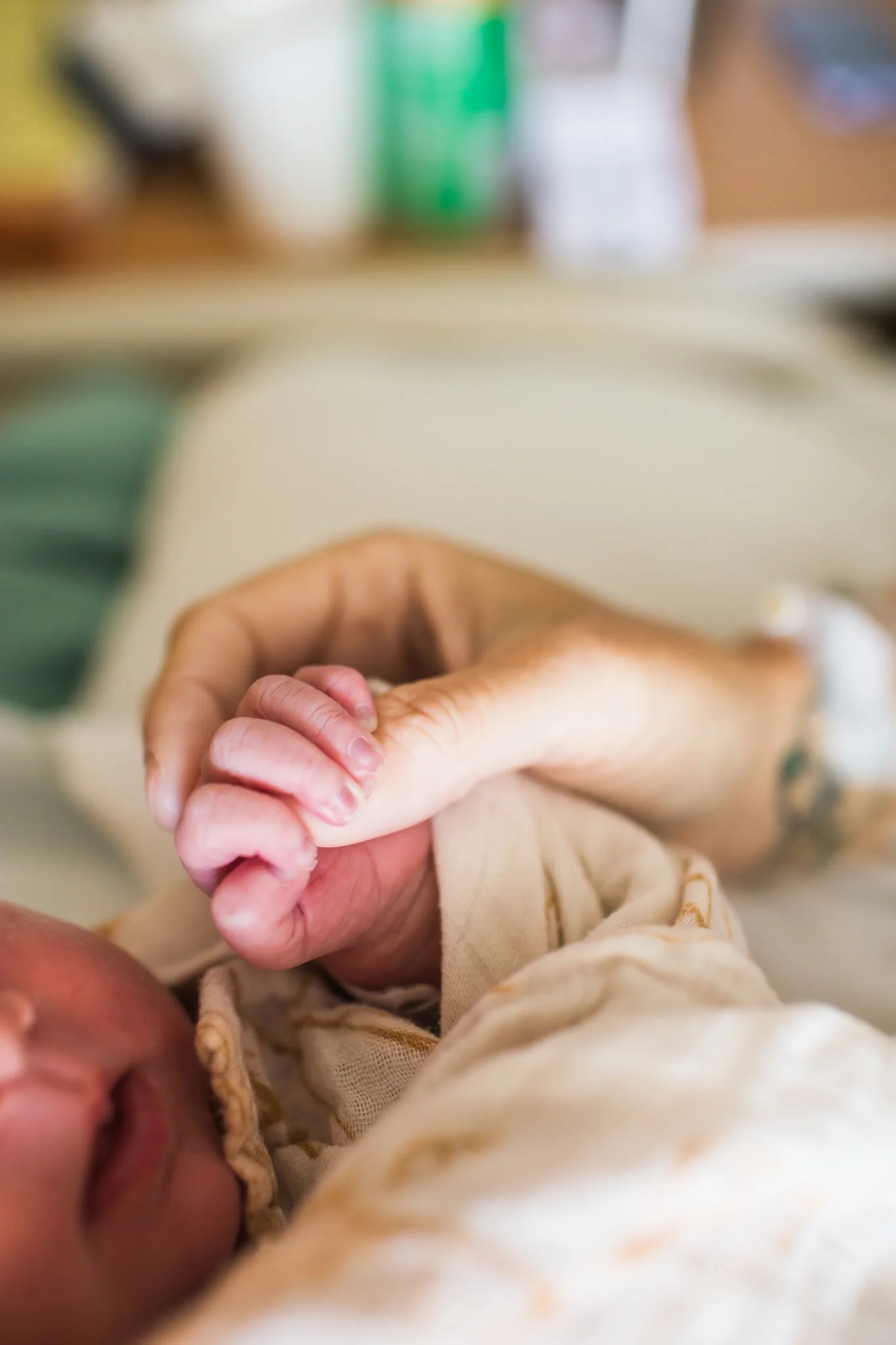 A close-up of a baby's hand held gently by an adult, with the adult's arm visible and the background blurred. birth-doula-newport-news-virginia-kinfolk-birth-co