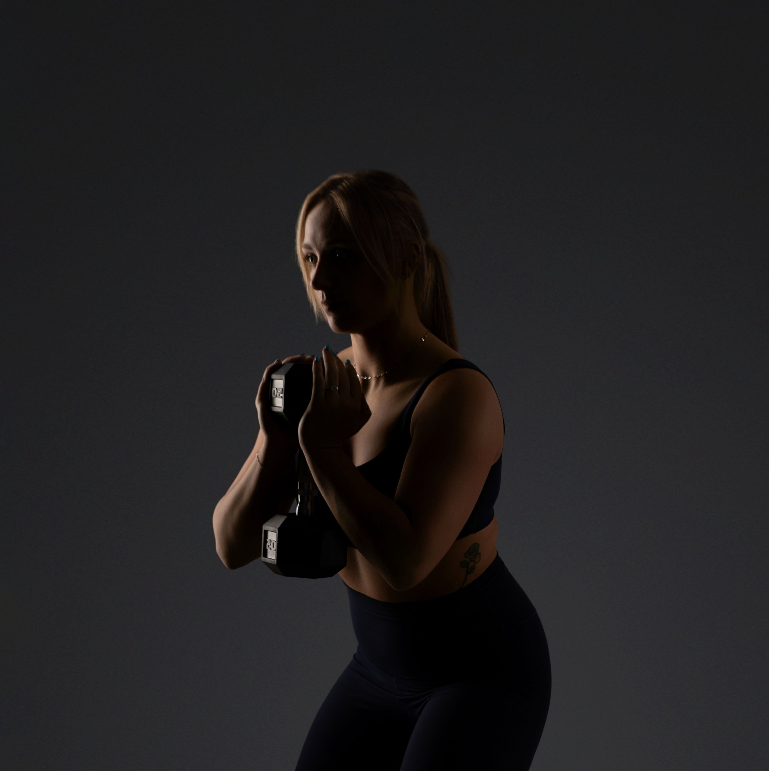 A woman with long blonde hair is holding a camera, partially seen from the side, against a dark background.