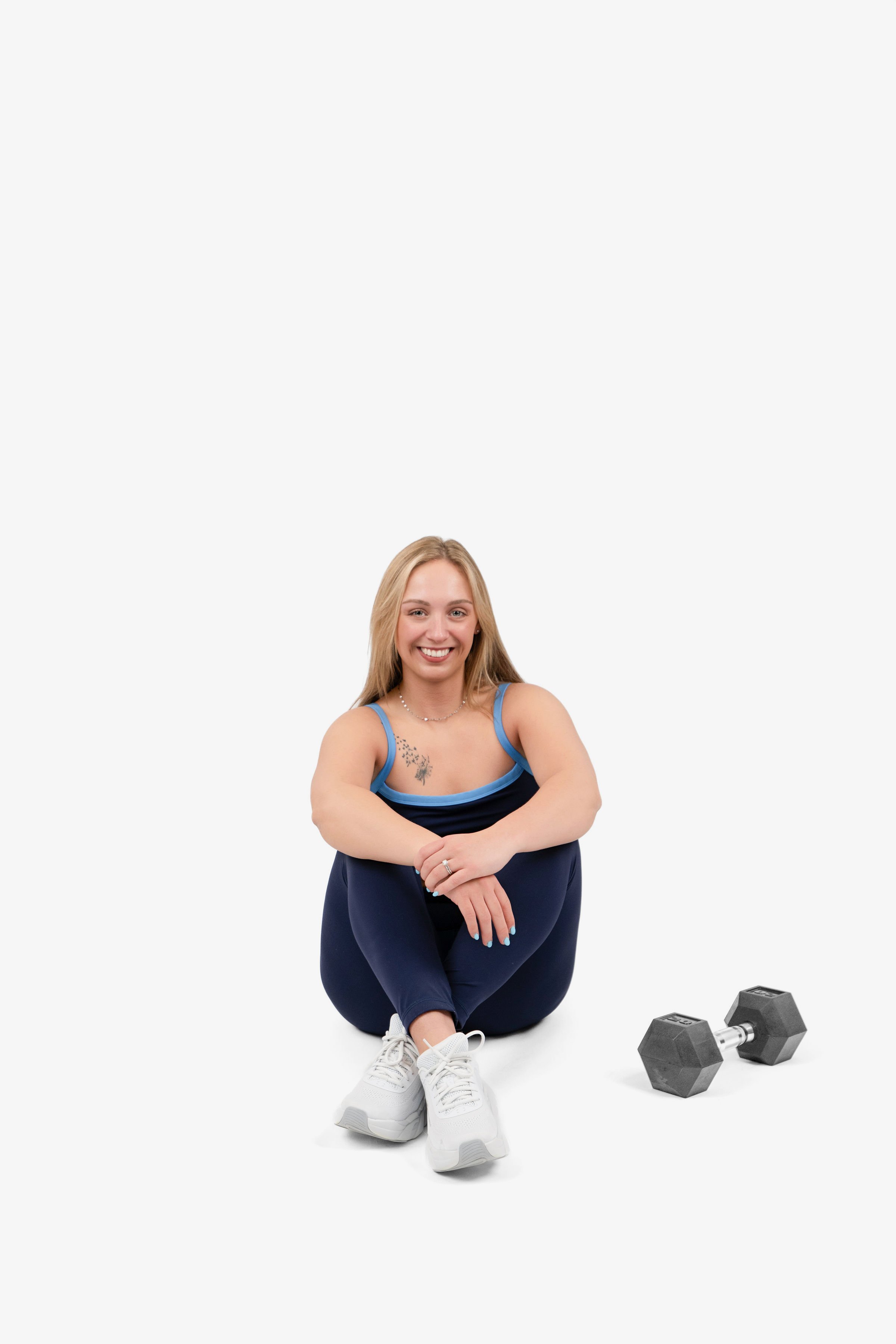 Smiling woman sitting on the floor with dumbbells and workout gear.