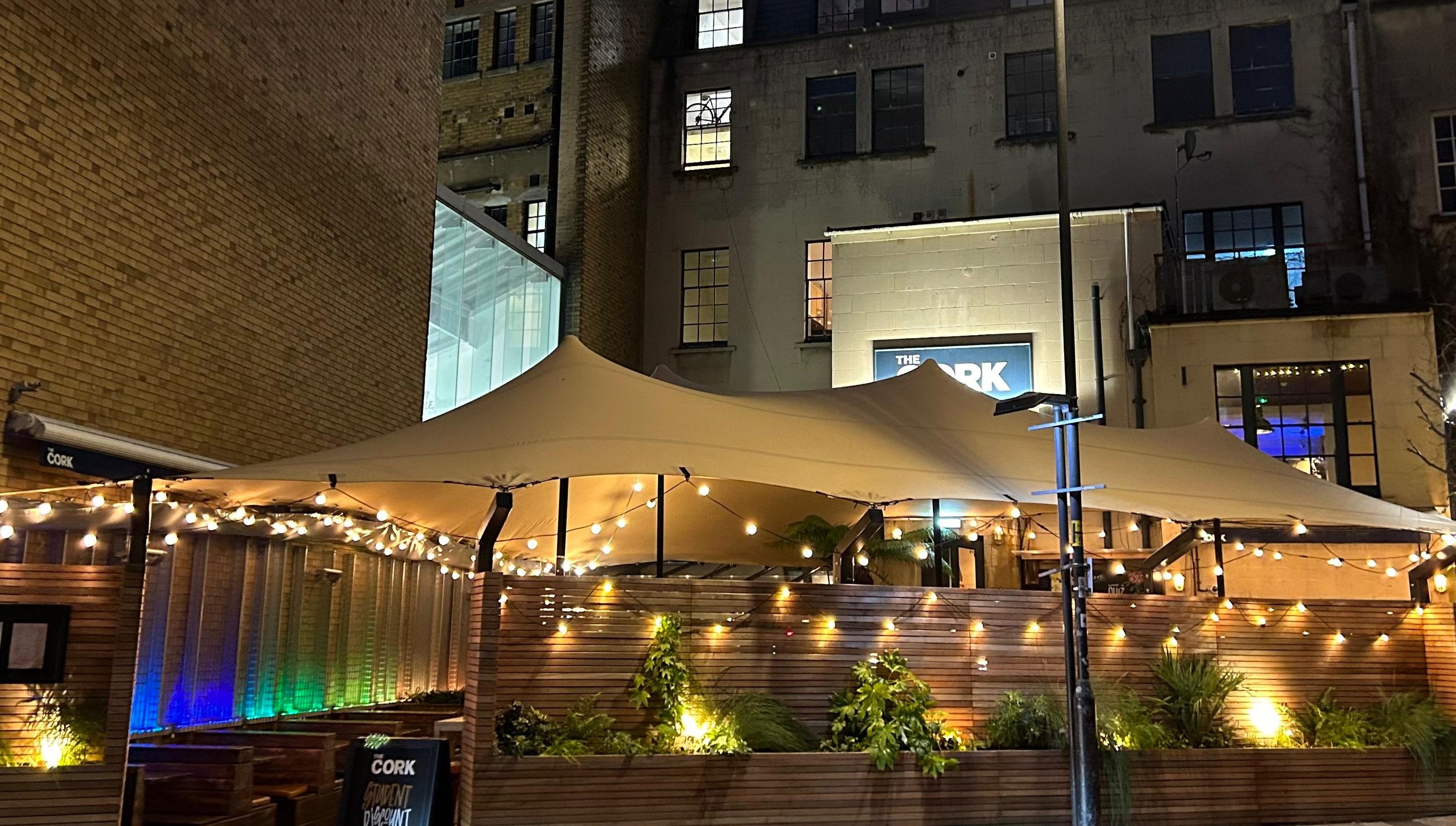 aPermanent stretch tent over the terrace at The Cork pub in Bath, lit with festoon lights at night