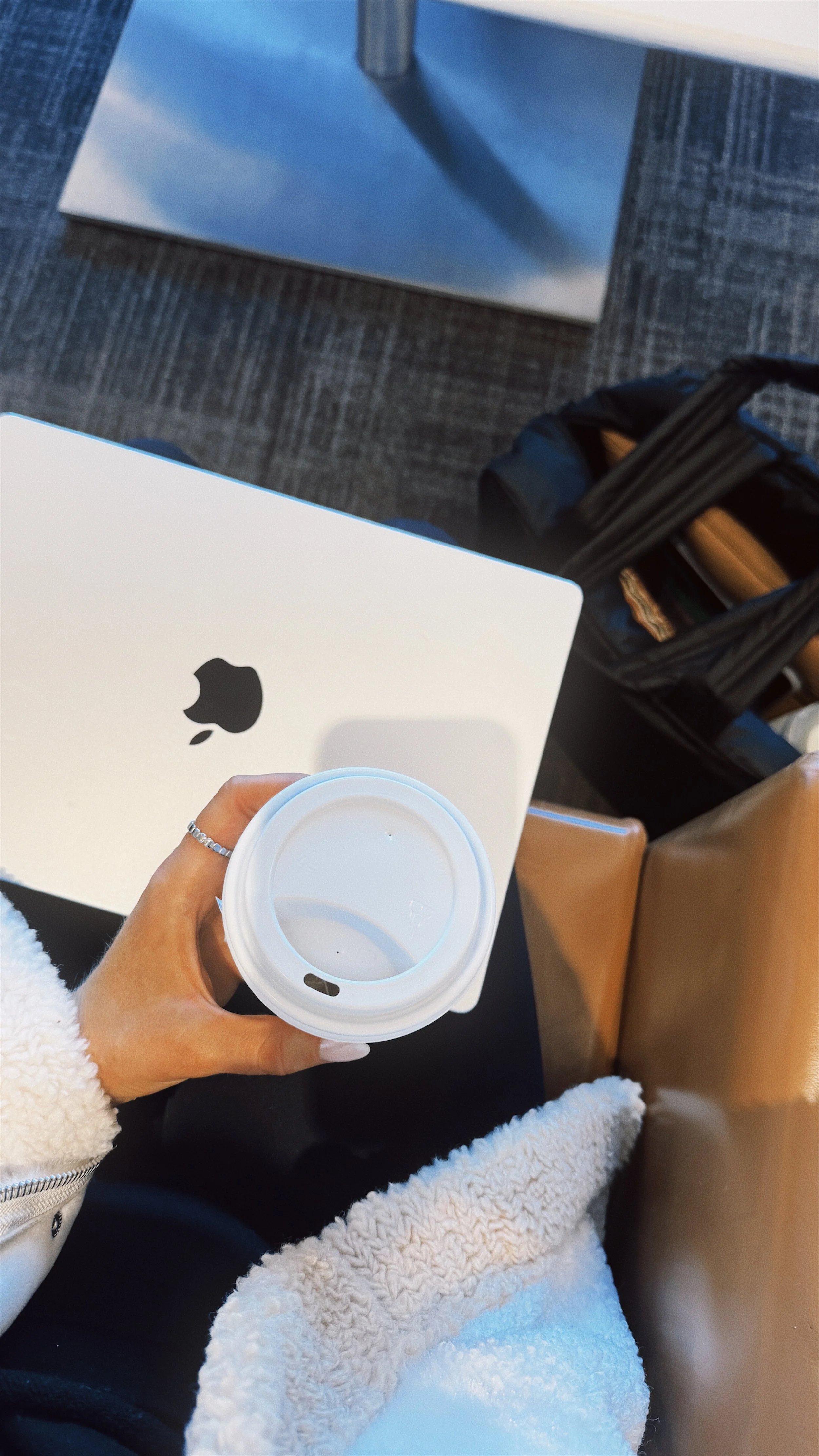 Person holding a coffee cup in an airport waiting area with a MacBook on their lap.