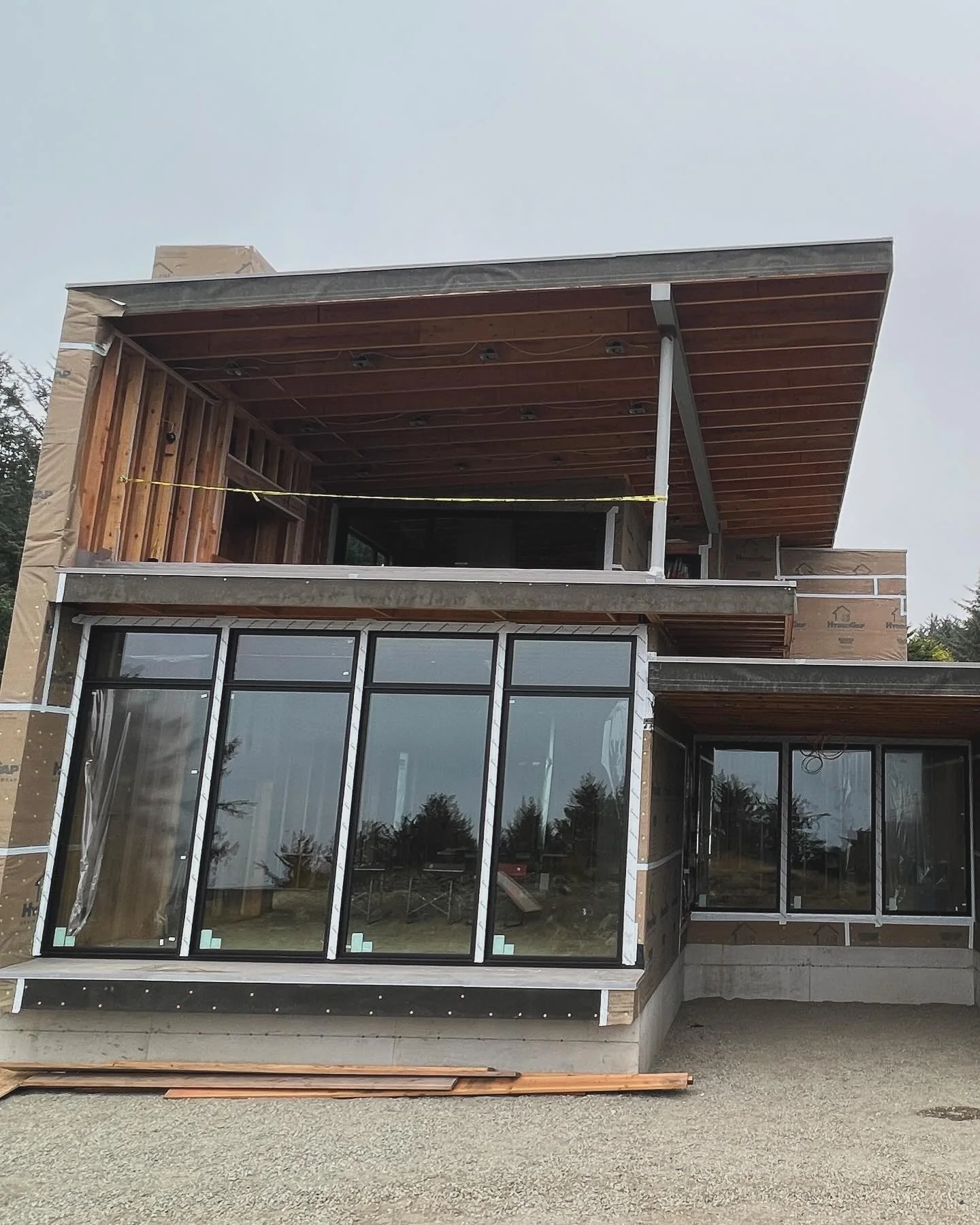 A building under construction with large glass windows on the ground floor and an open upper floor with wooden ceiling and walls.