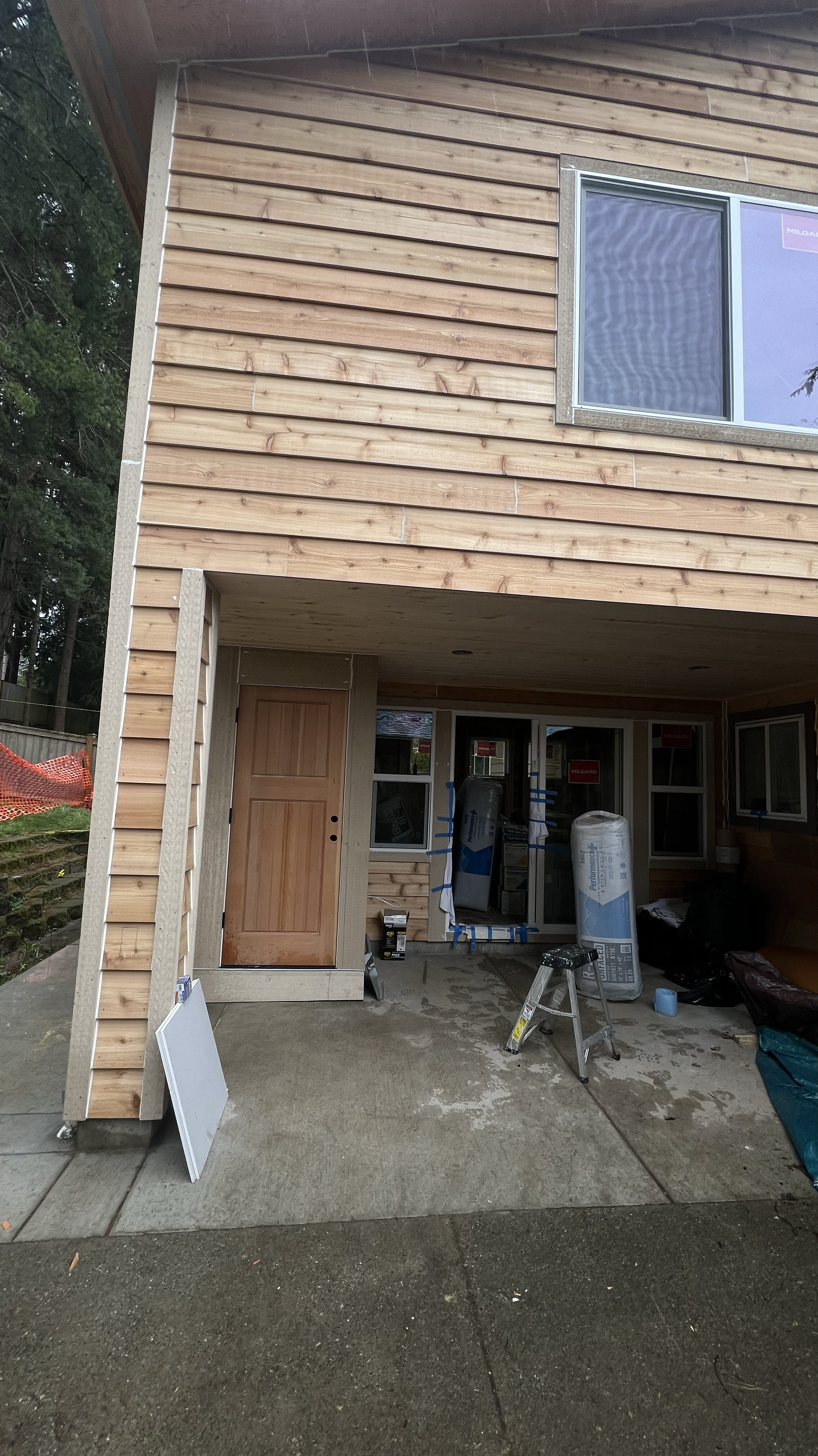Construction site of a two-story wooden house with an unfinished front porch and tools scattered around.