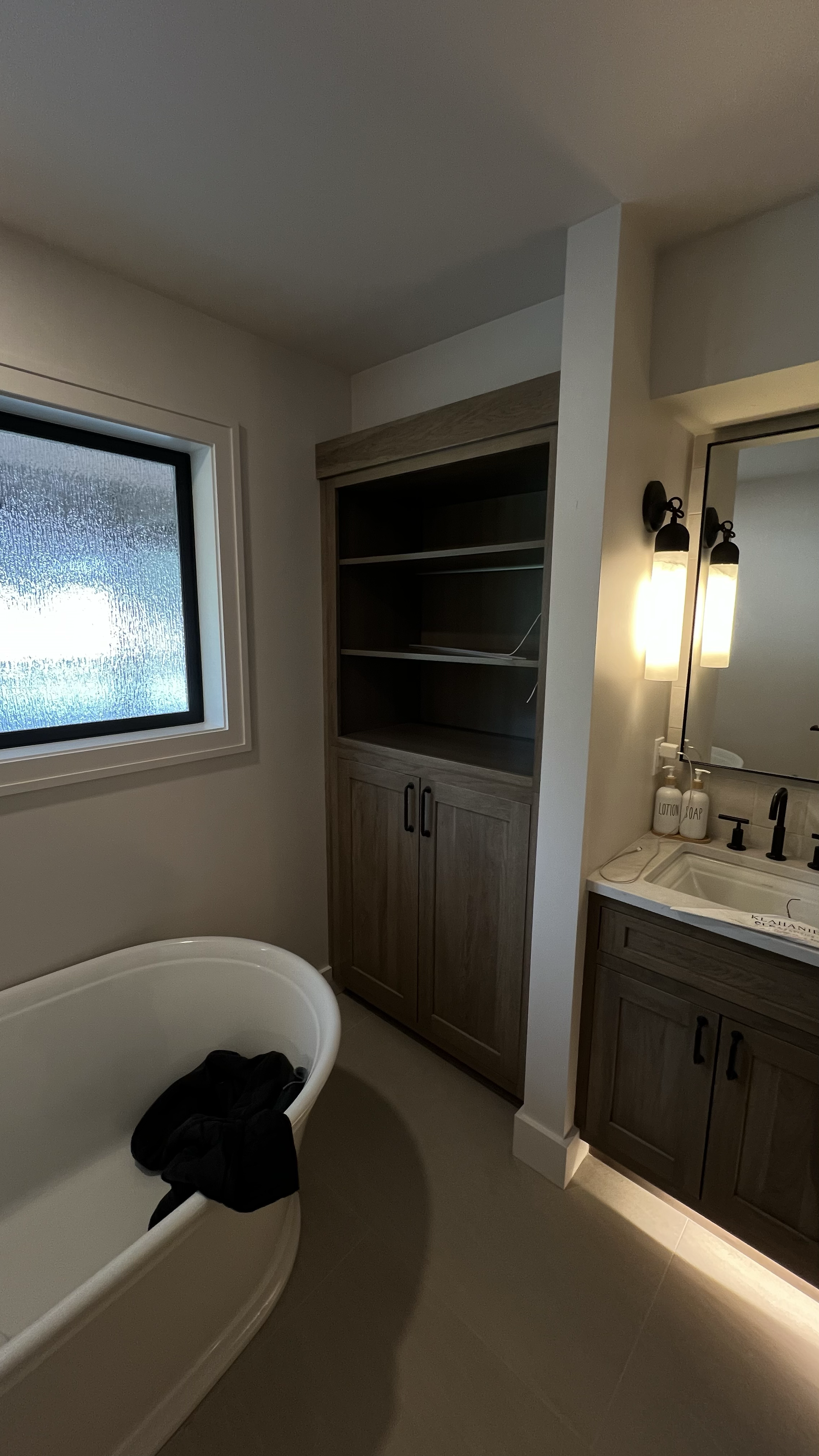 Bathroom with a bathtub, a window with frosted glass, a wooden cabinet, and a sink with a mirror and wall-mounted lights.