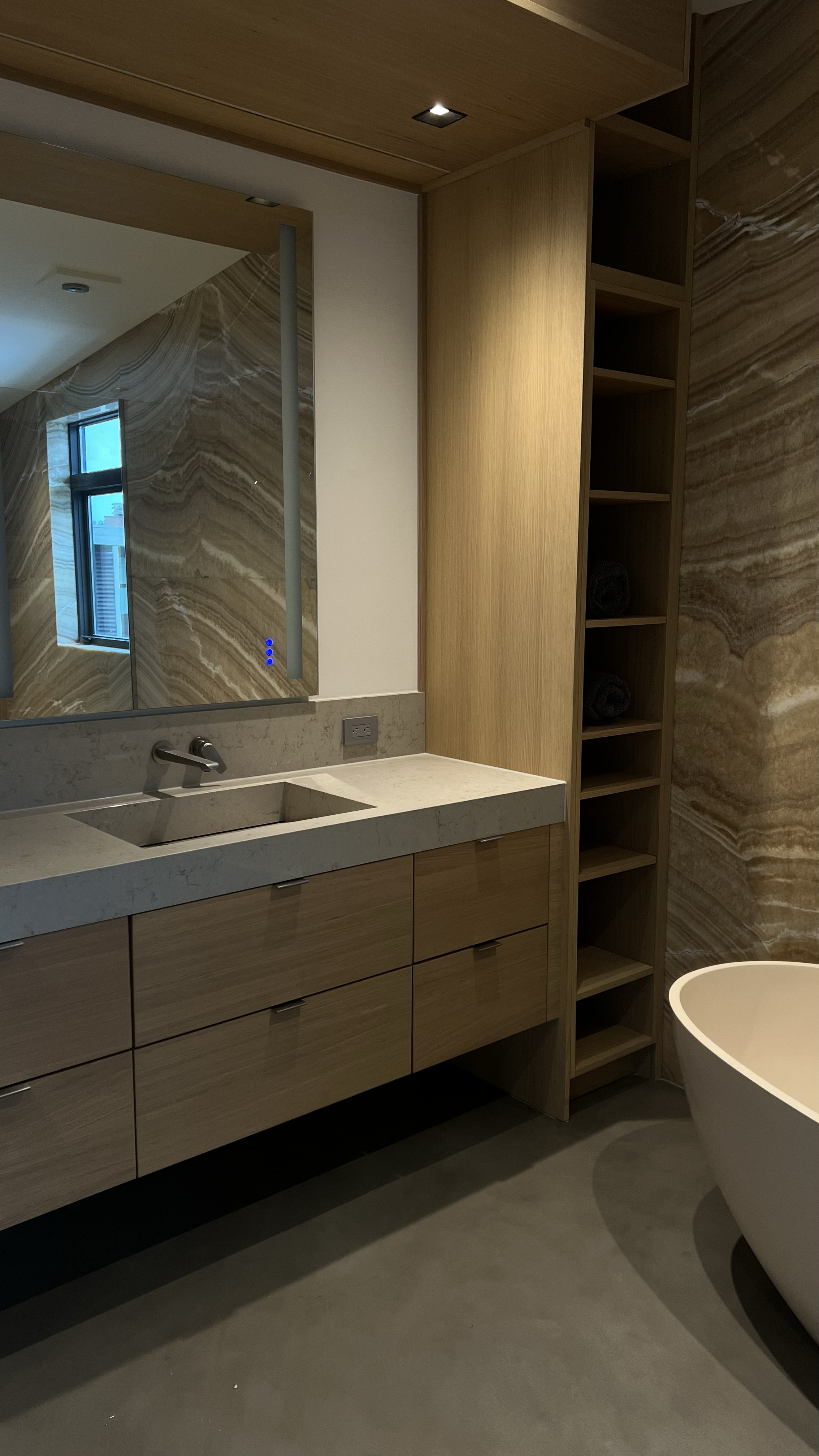 Modern bathroom with a wooden vanity, marble countertop, large mirror, and a bathtub.