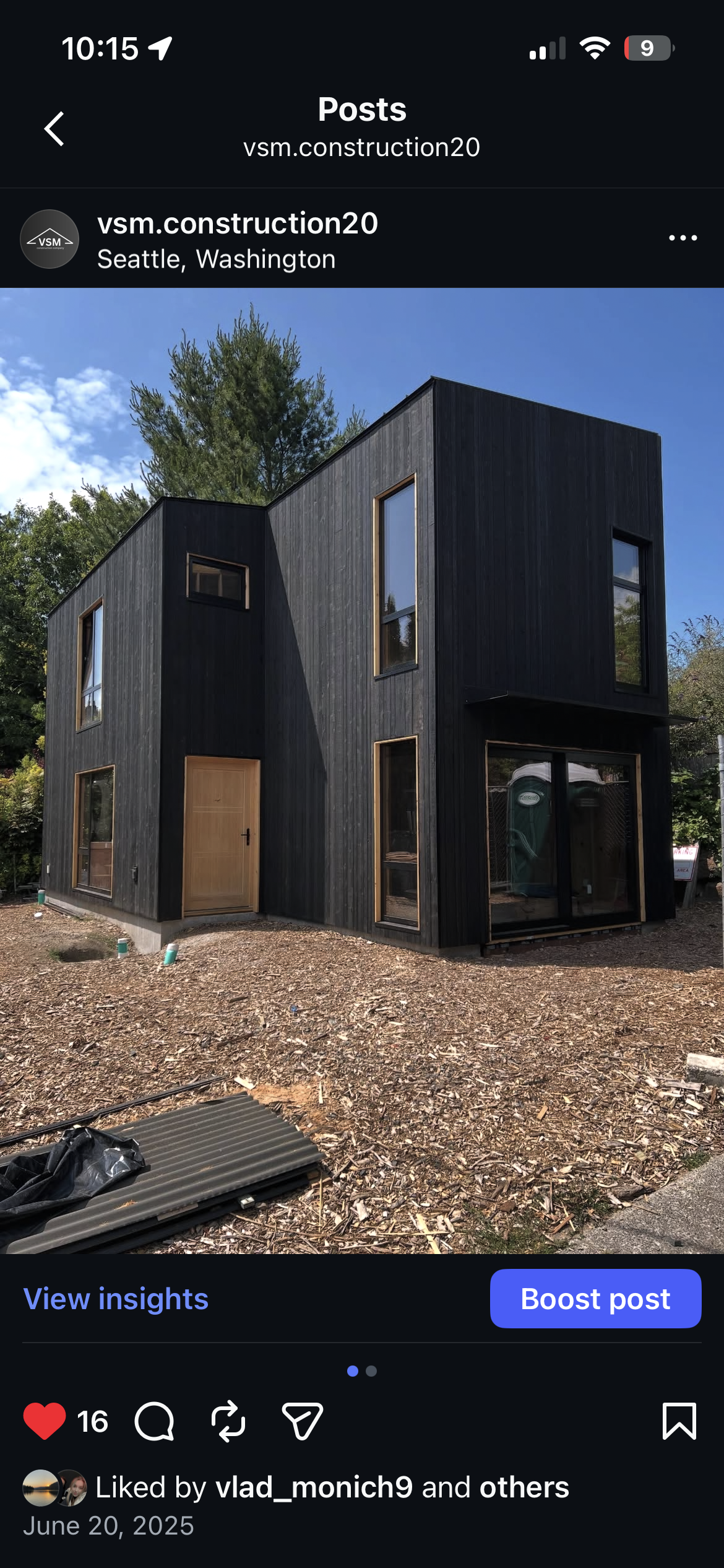 A modern two-story black wooden house under construction in Seattle, Washington, with multiple windows and a wooden front door, surrounded by construction materials and dirt.