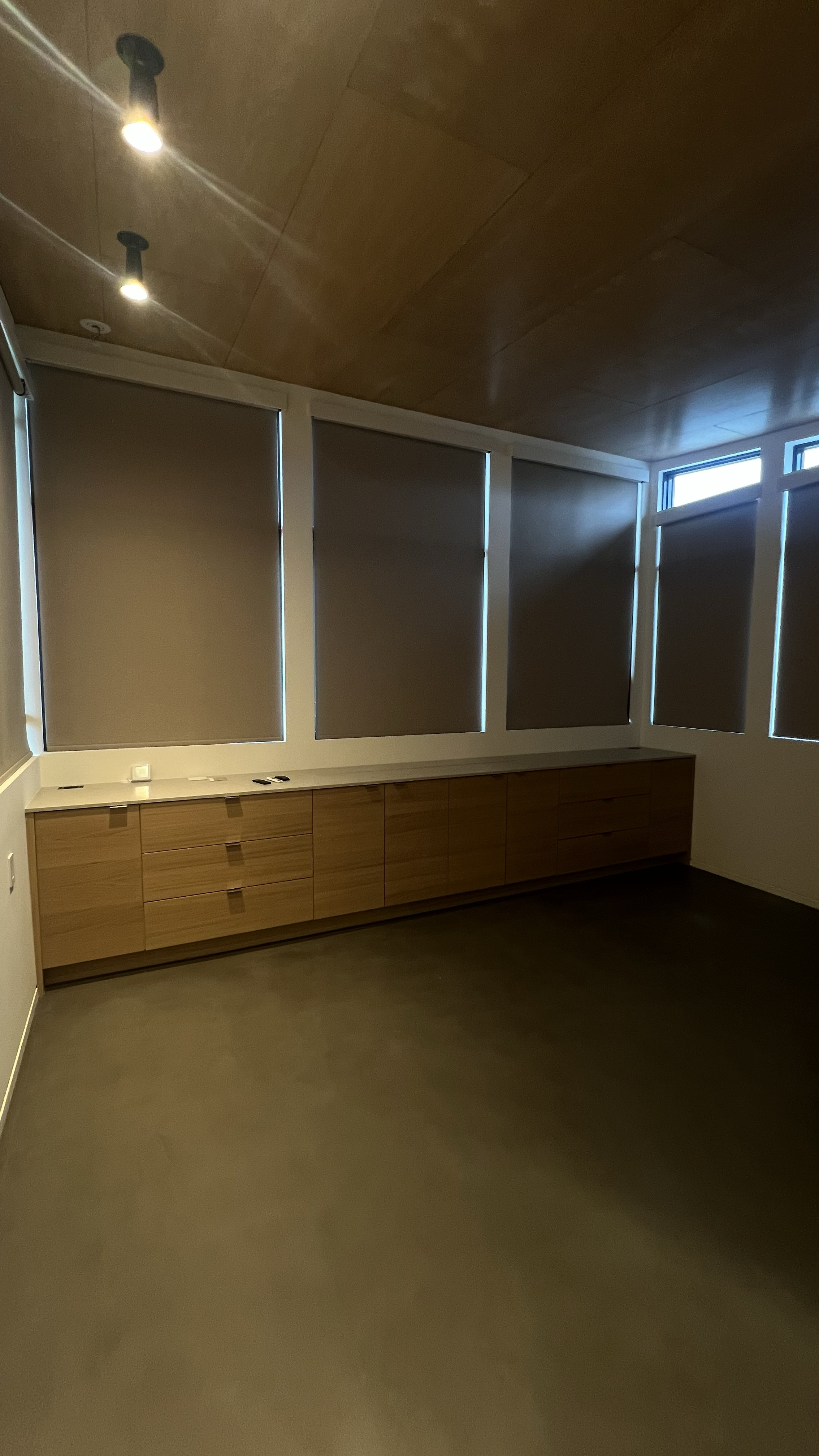 Empty room with wooden cabinet, closed window blinds, and ceiling lights.