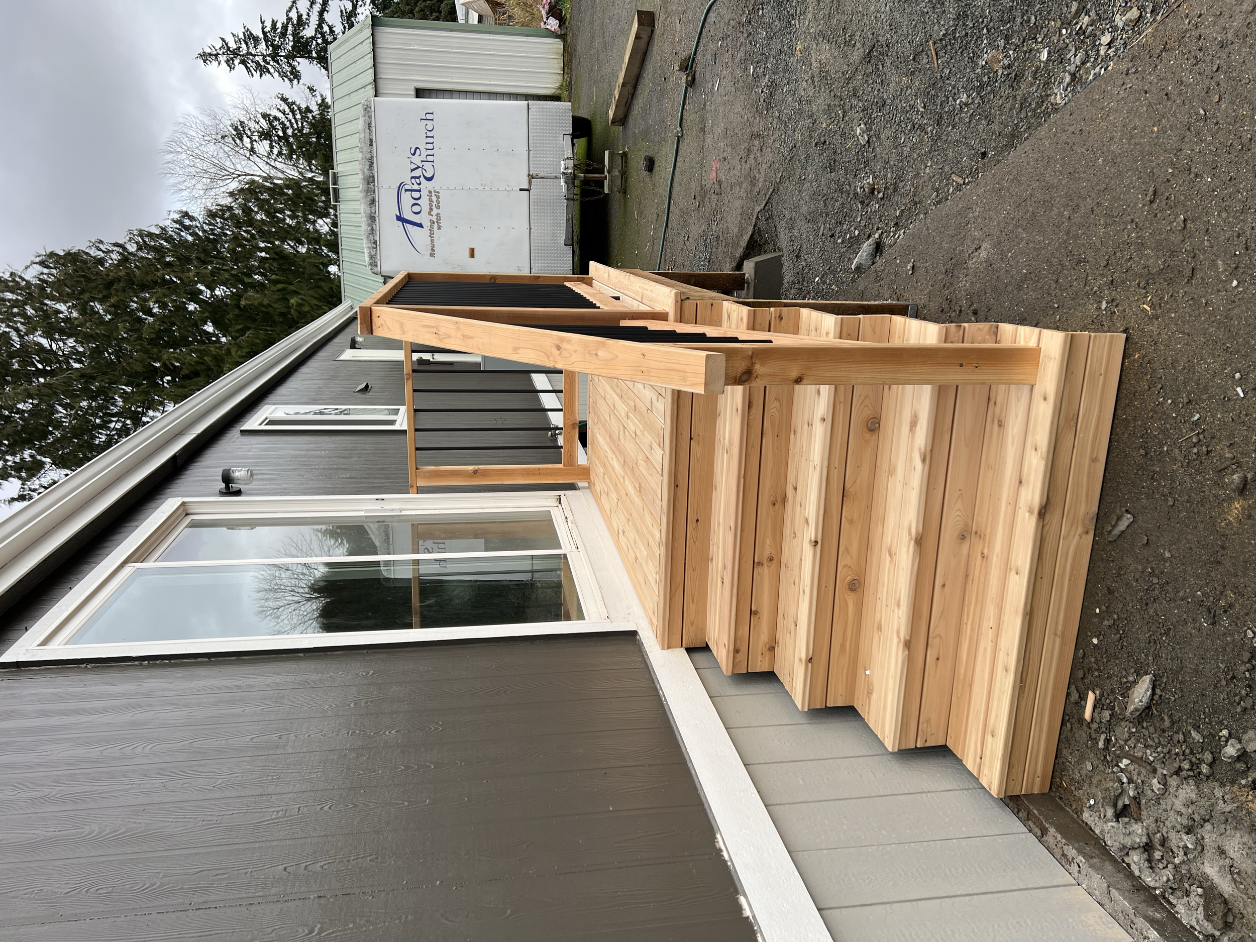 New wooden staircase leading up to a sliding glass door on the exterior of a gray building.