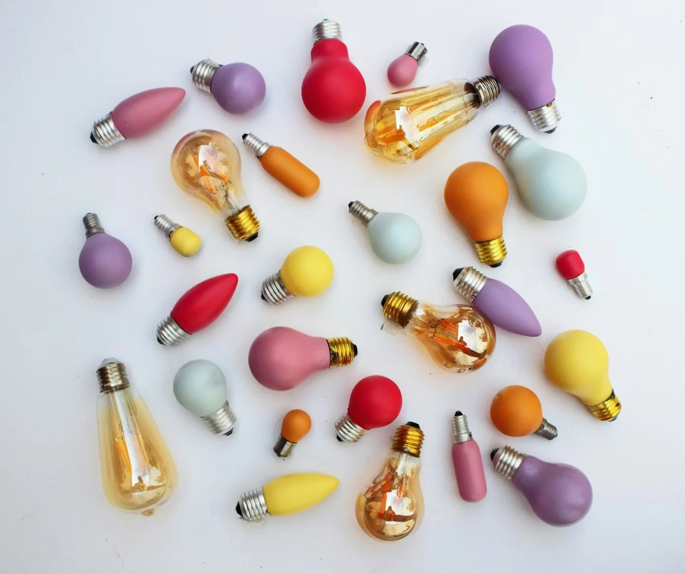 Various colorful light bulbs and lamp accessories scattered on a white surface.