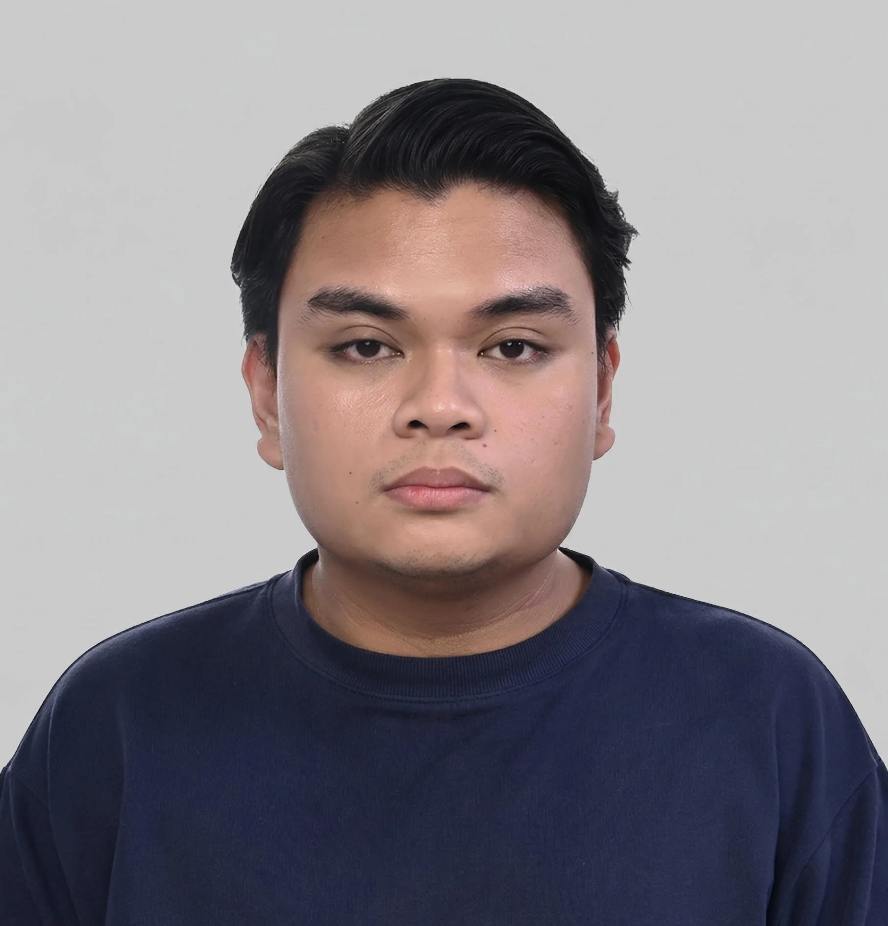 A young man with black hair in a navy blue shirt, facing the camera against a plain light gray background.