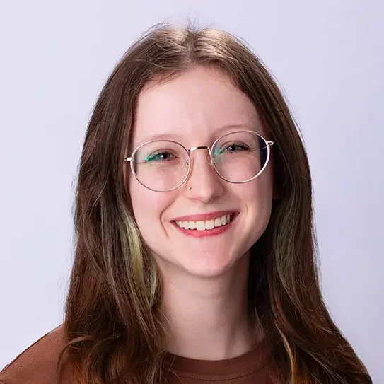A young woman with long light brown hair, round glasses, and a brown shirt smiling at the camera.