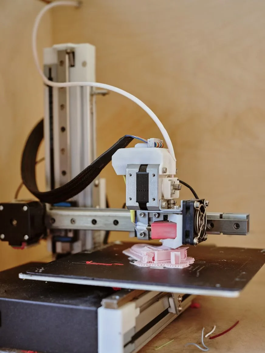 A 3D printer creating a pink object on its black printing bed.