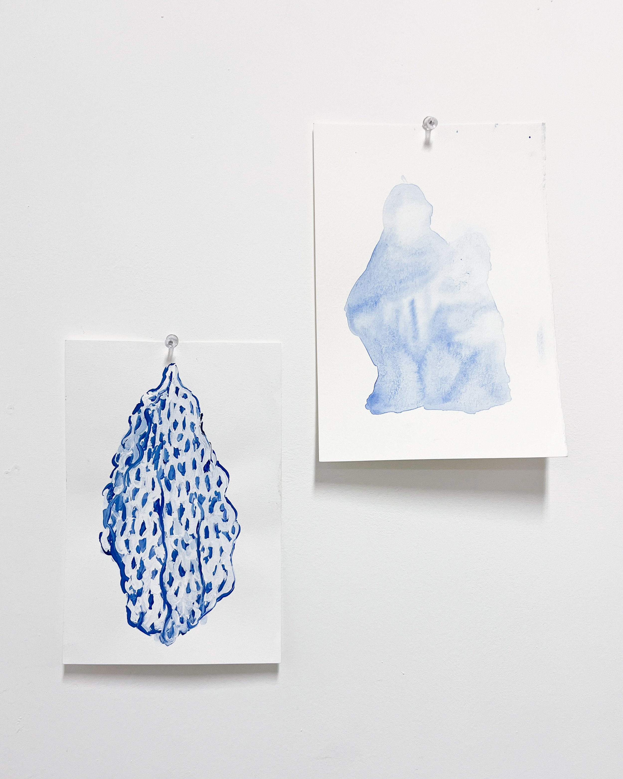 Two blue abstract watercolor art pieces hung on a white wall with push pins.