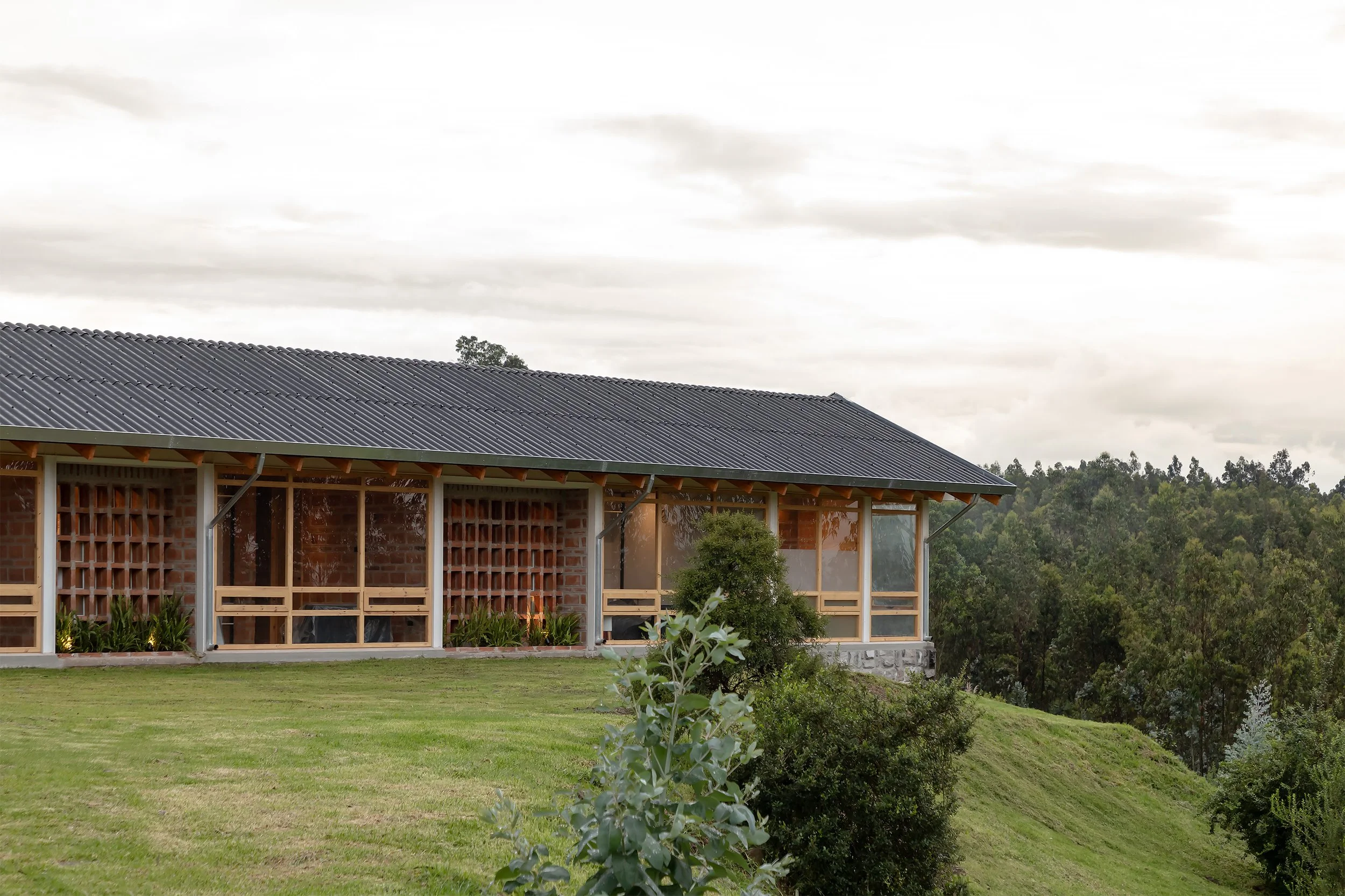 Casa de construcción moderna con techo de lámina metálica, rodeada de vegetación y árboles, con cielo nublado.