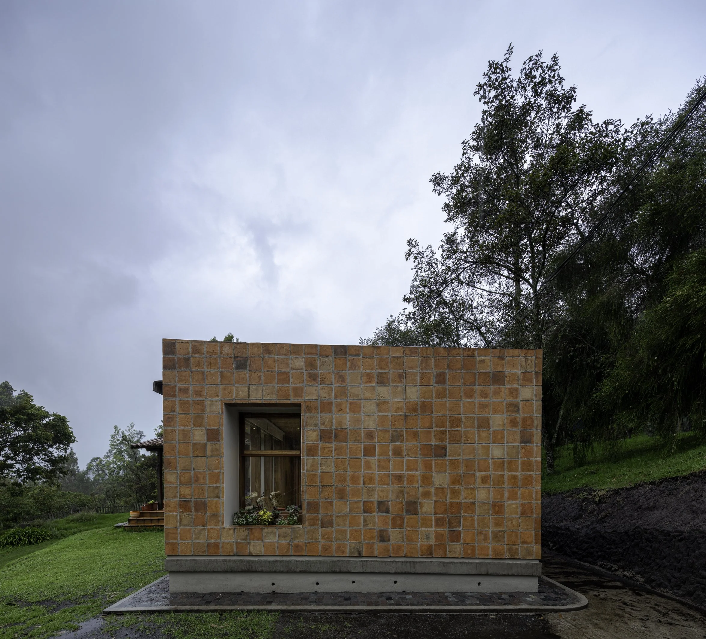 Casa moderna de ladrillos con un gran ventanal en un entorno verde con árboles y césped.