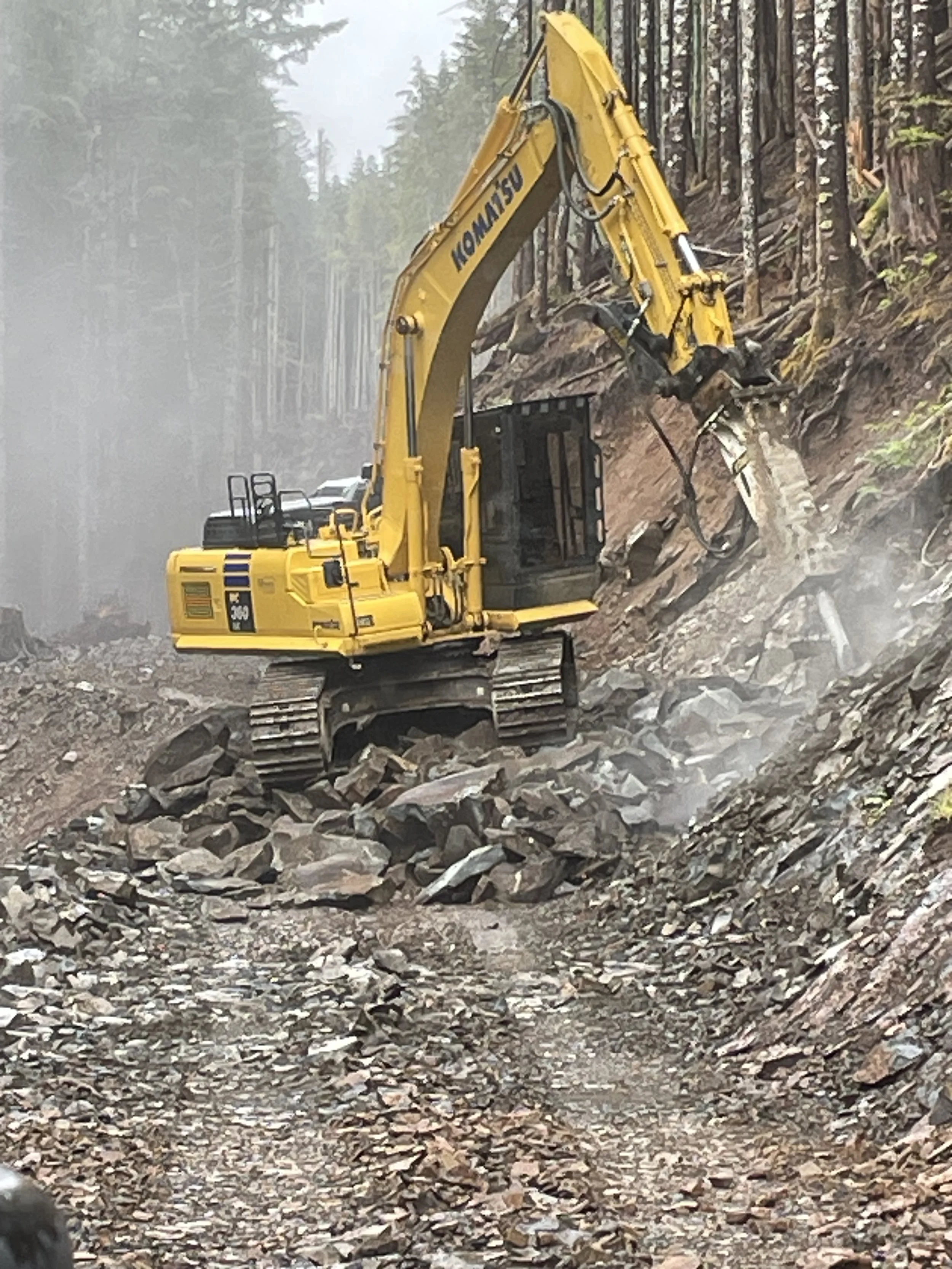 Komatsu excavator working on a rocky, forested hillside