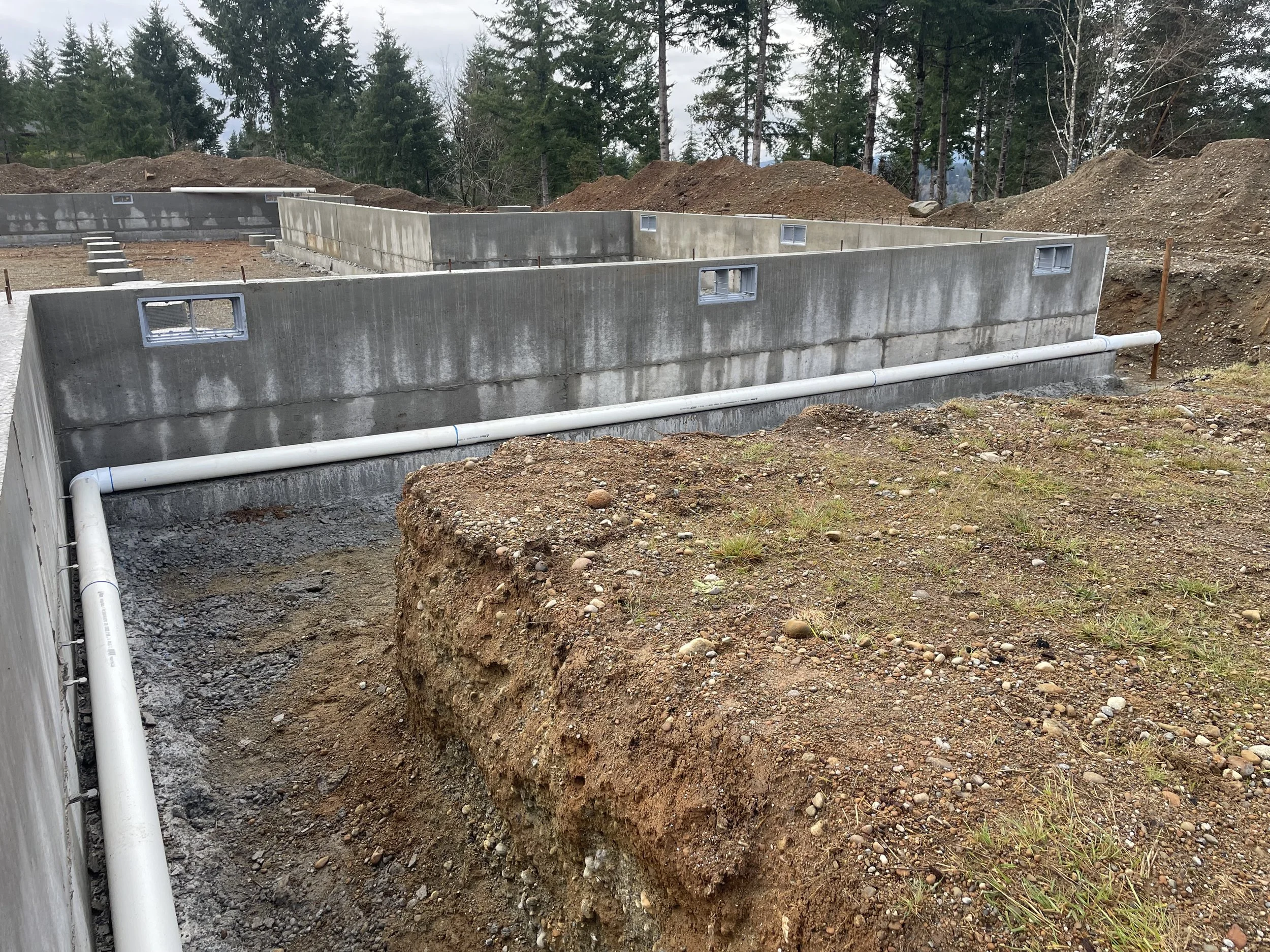 Site prep: concrete foundation walls after cut out.  PVC pipes laid, prior to backfill
