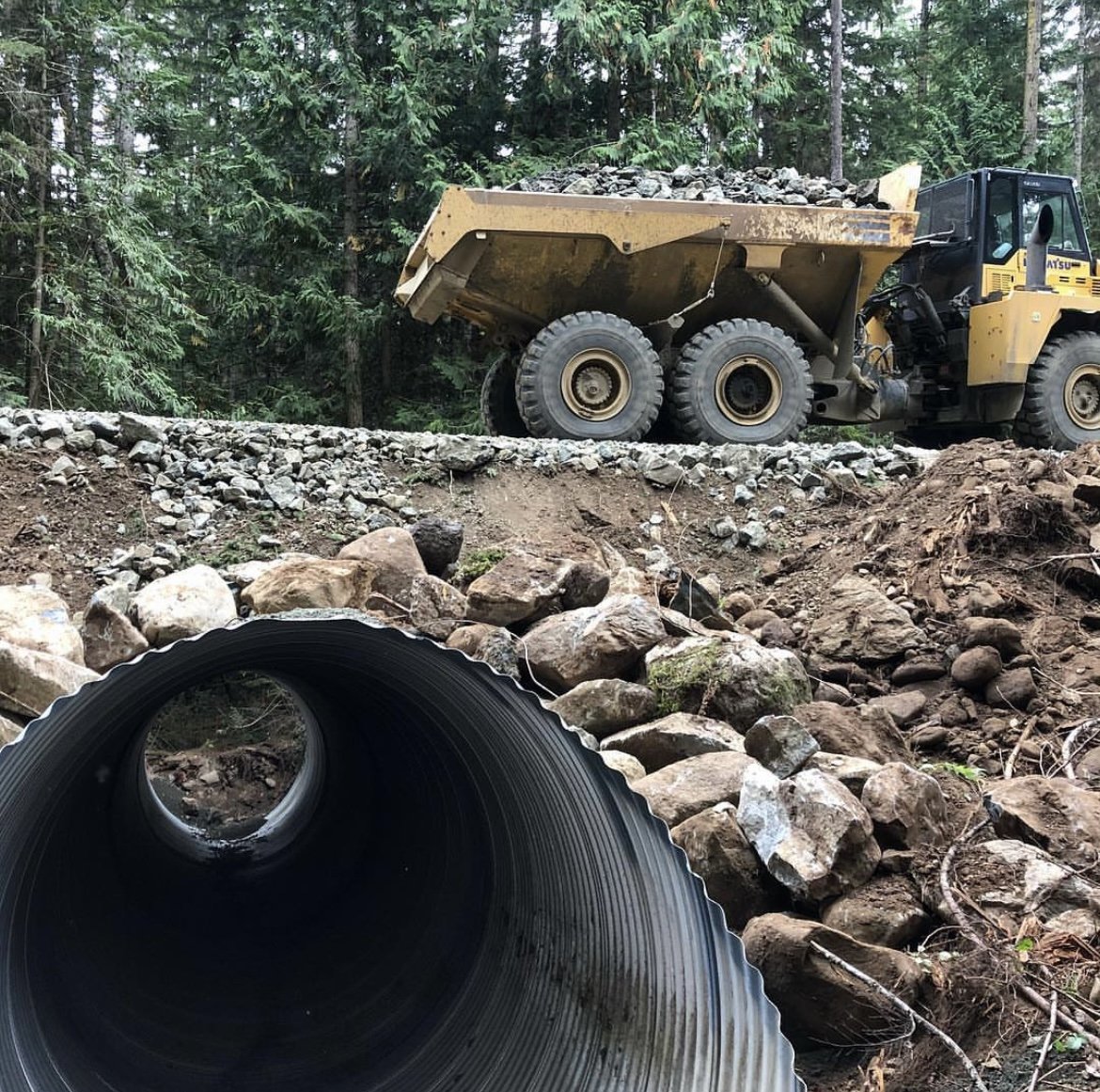 Dump Truck Hauling rock over a recently installed large culvert on a Timber Land Road project