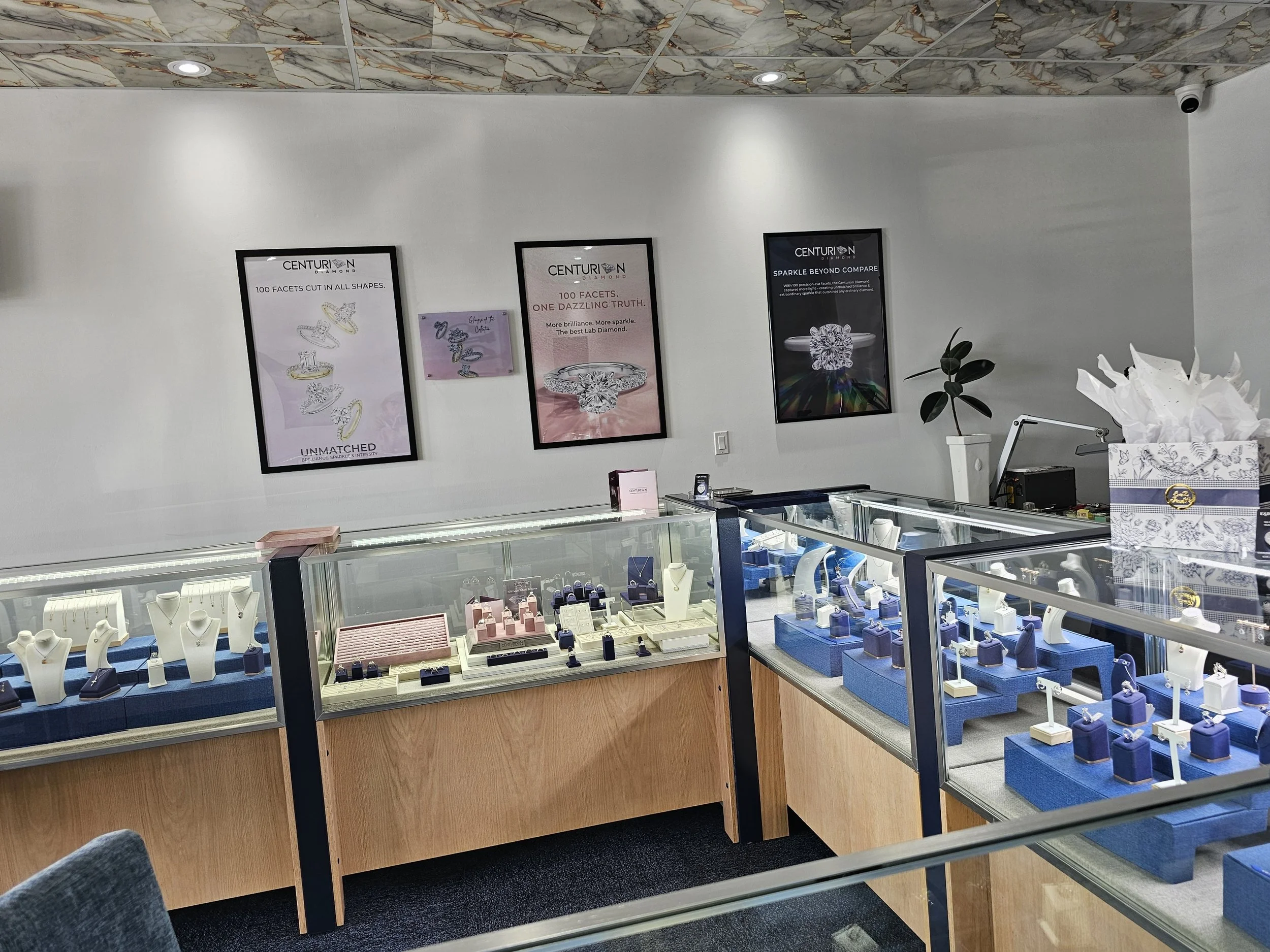 Display cases filled with jewelry, with posters of jewelry advertisements on the wall behind. The posters feature diamond rings and phrases like '100 facets cut in all shapes' and 'Sparkle beyond compare.'