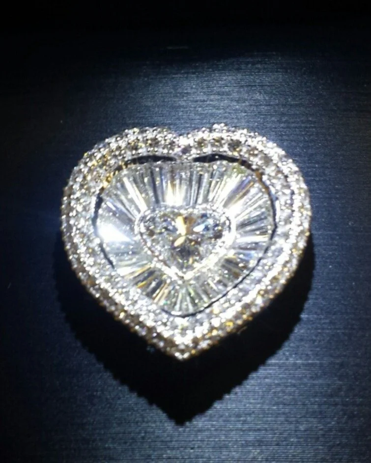 A heart-shaped 14 kt white gold pendant with a heart shaped natural diamond in the center, decorated with numerous small banquettes diamonds with halo diamond around it