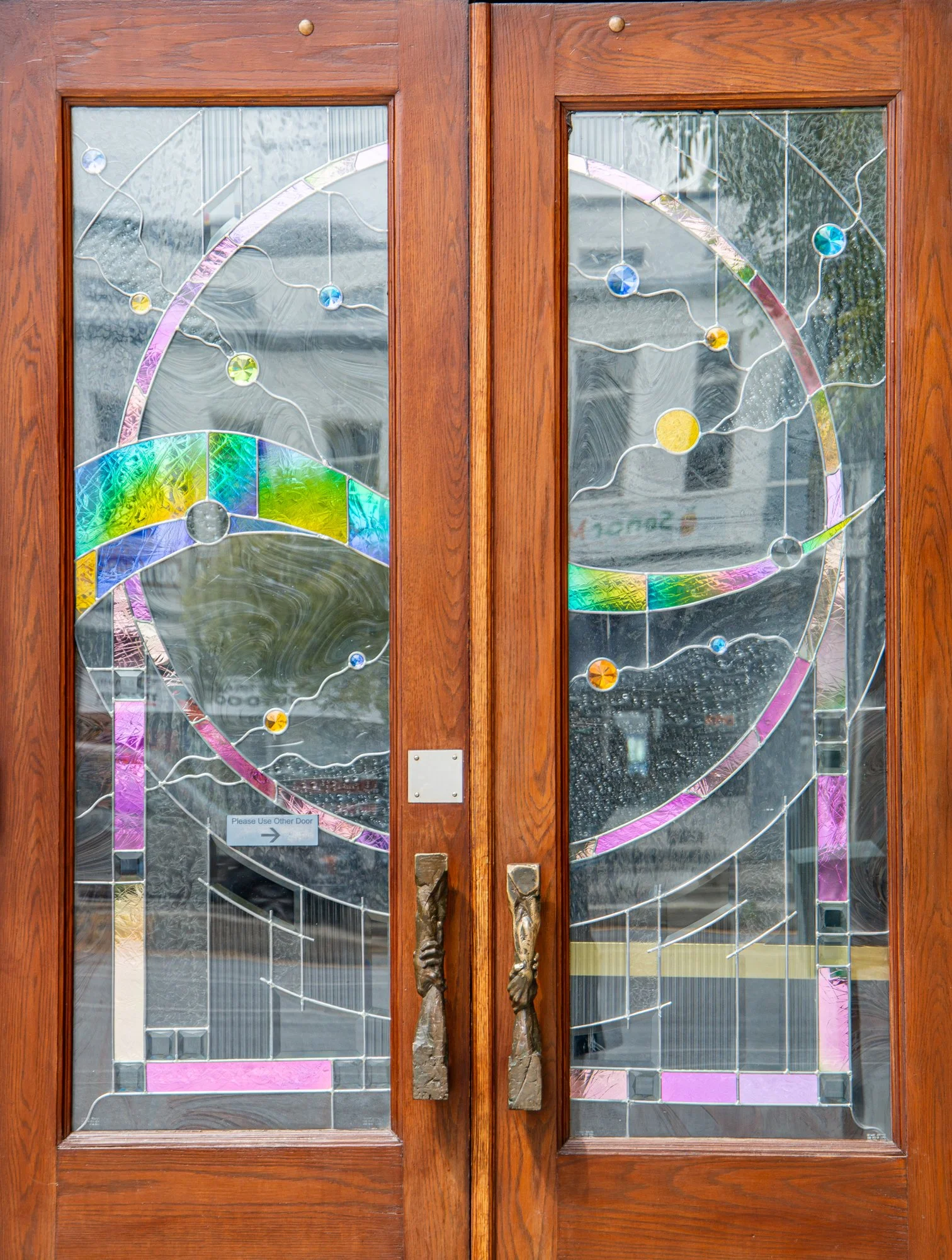 Wooden double doors with decorative stained glass panels featuring abstract patterns and colorful circles.
