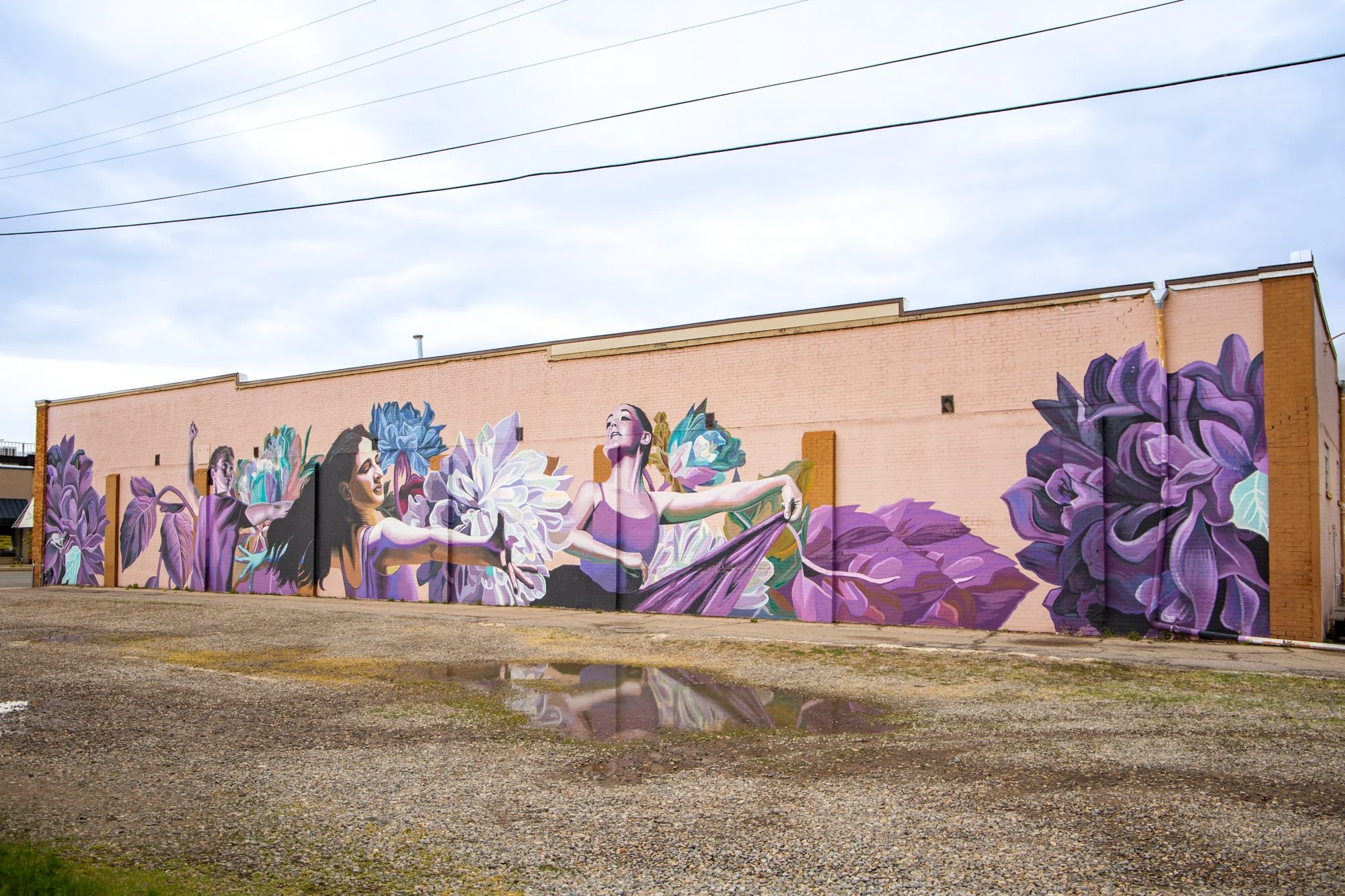 Colorful mural of three ballet dancers with purple and blue flowers on a brick building