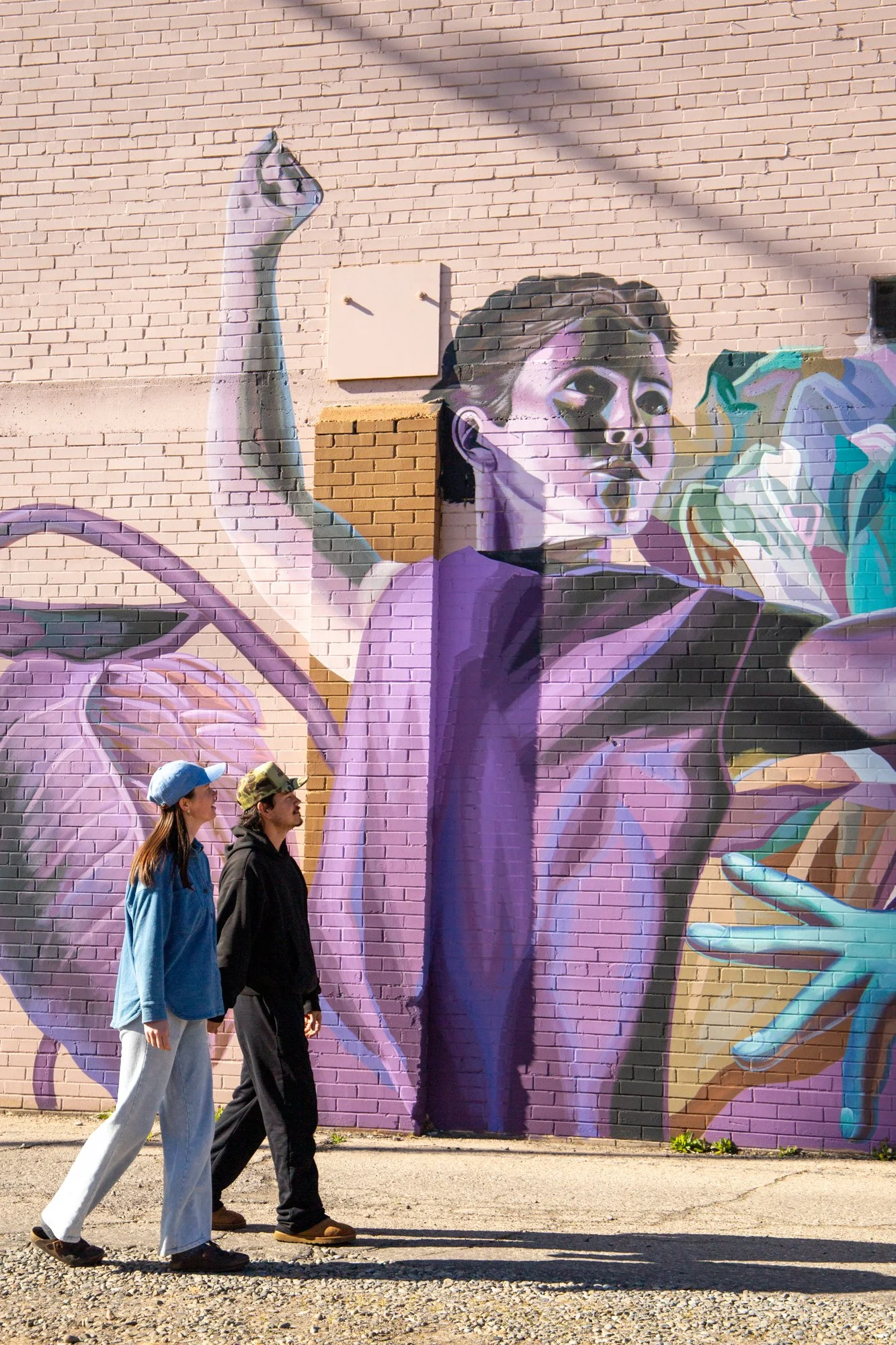 Street scene with a colorful mural of a woman dancing, and two people walking past in front of the mural.