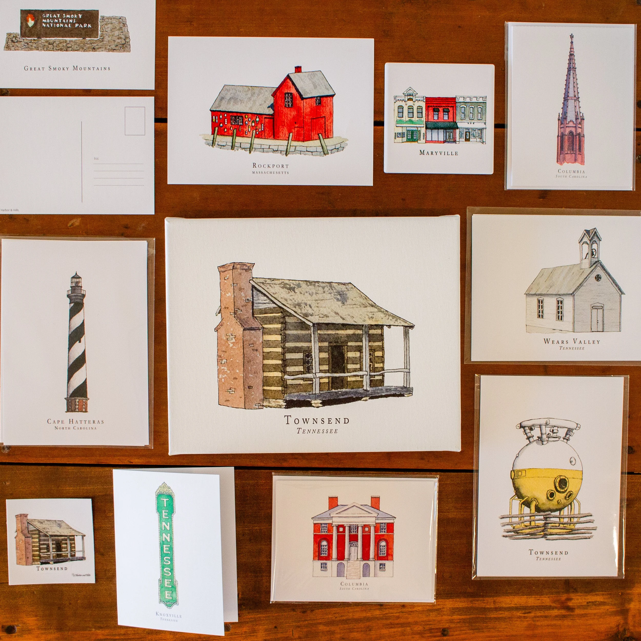 A display of illustrated postcards featuring landmarks from towns in Tennessee, South Carolina, North Carolina, and Massachusetts, including a red barn, a church steeple, a lighthouse, and historic buildings.