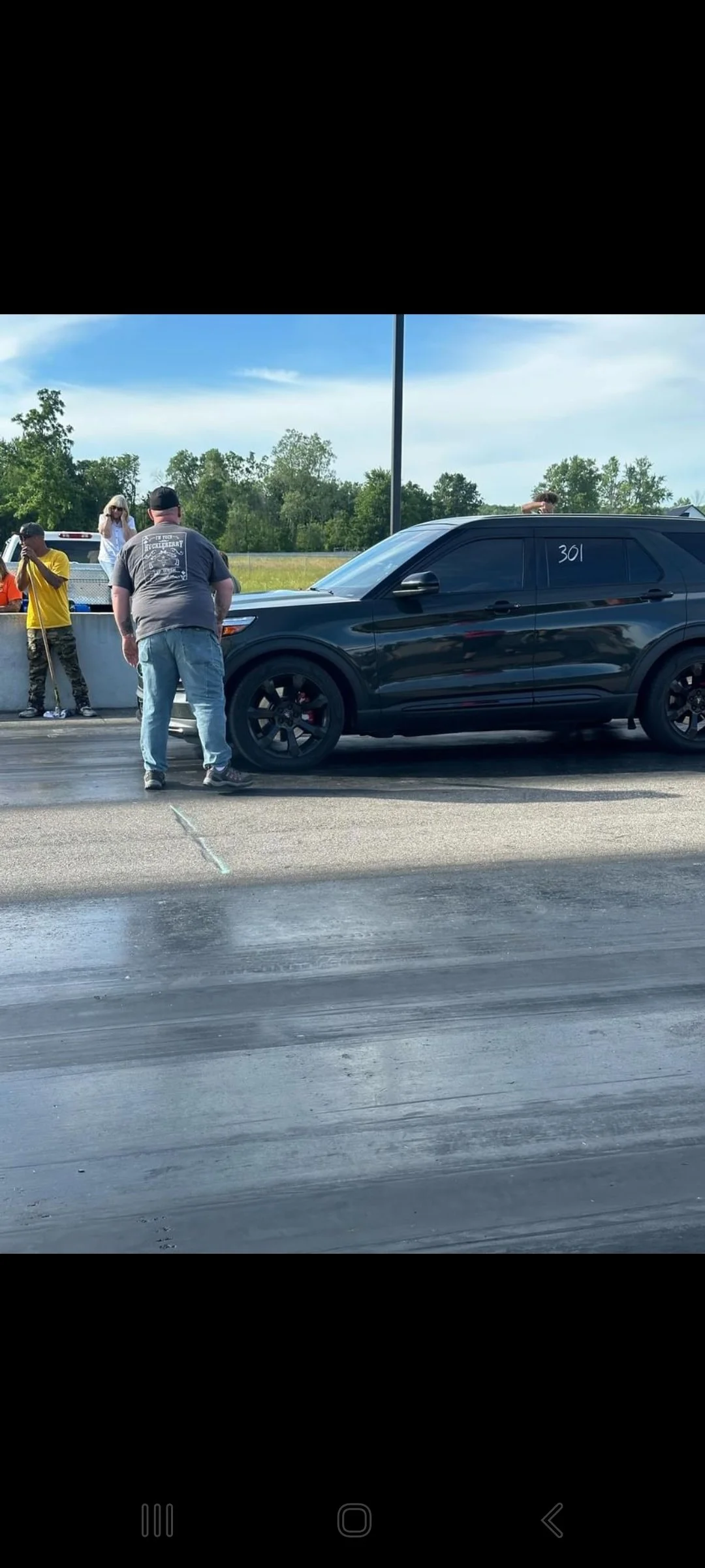 Black SUV with the number 301 written on the window, staging on a drag strip, with people standing nearby.