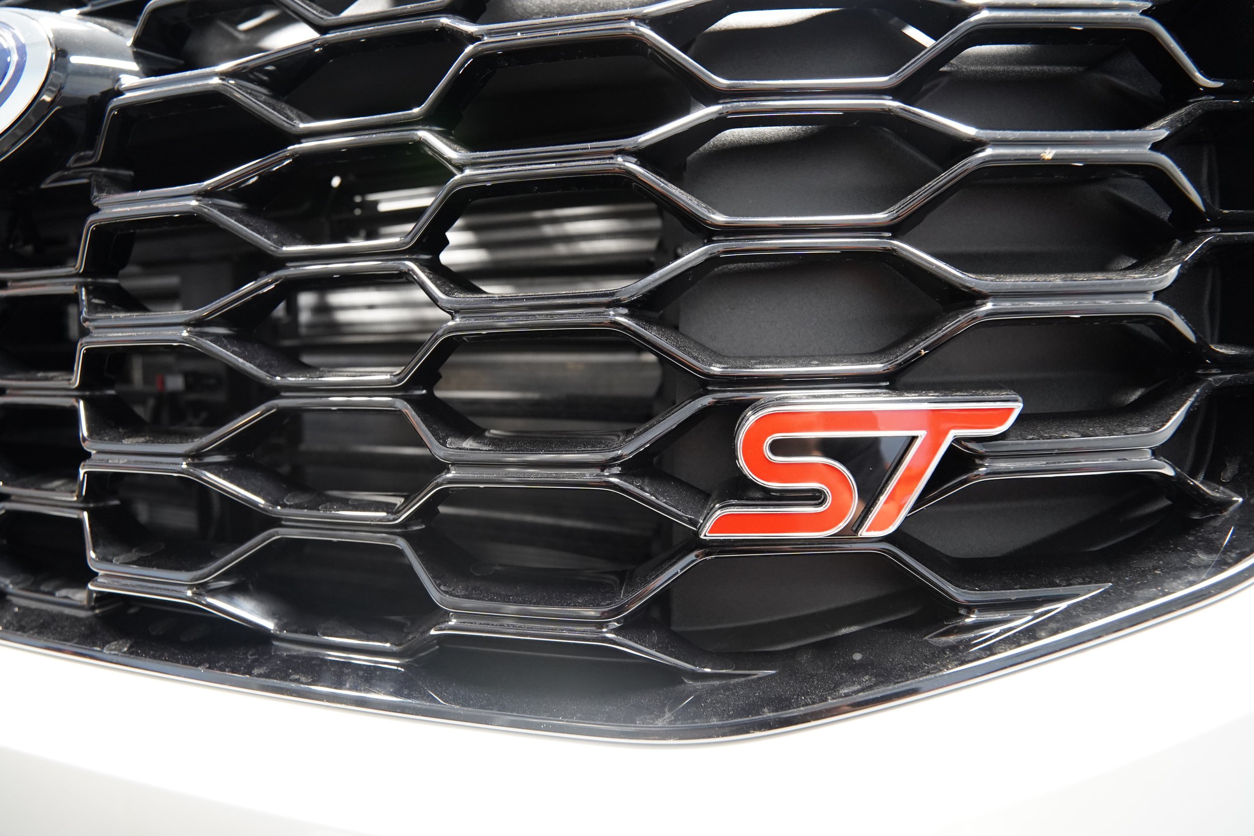Close-up of a car grille with a red 'ST' badge in the center.