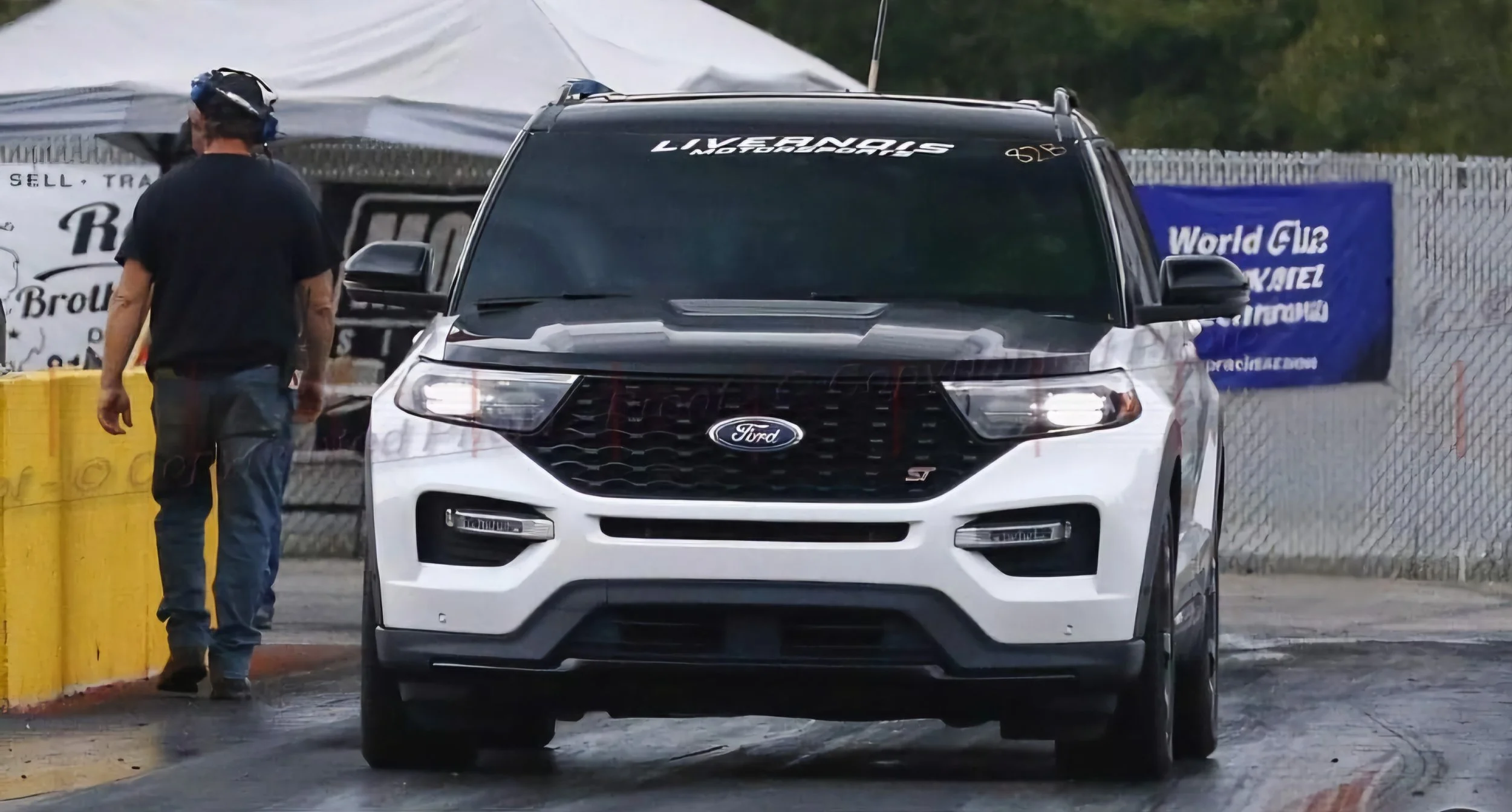 White Ford SUV at a drag racing event with a man in black shirt and jeans standing nearby.